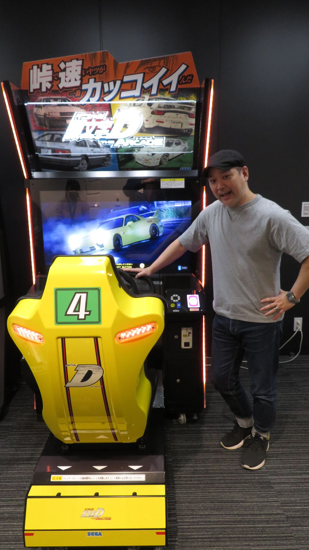 新作筐体の横でポーズを取る新井氏