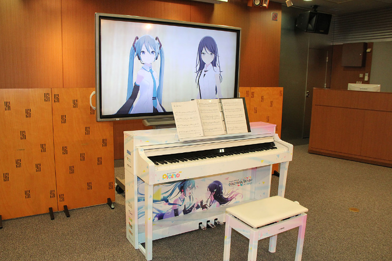 約60インチクラスのモニターが置かれ、画面にはミクさんと一歌が映っている