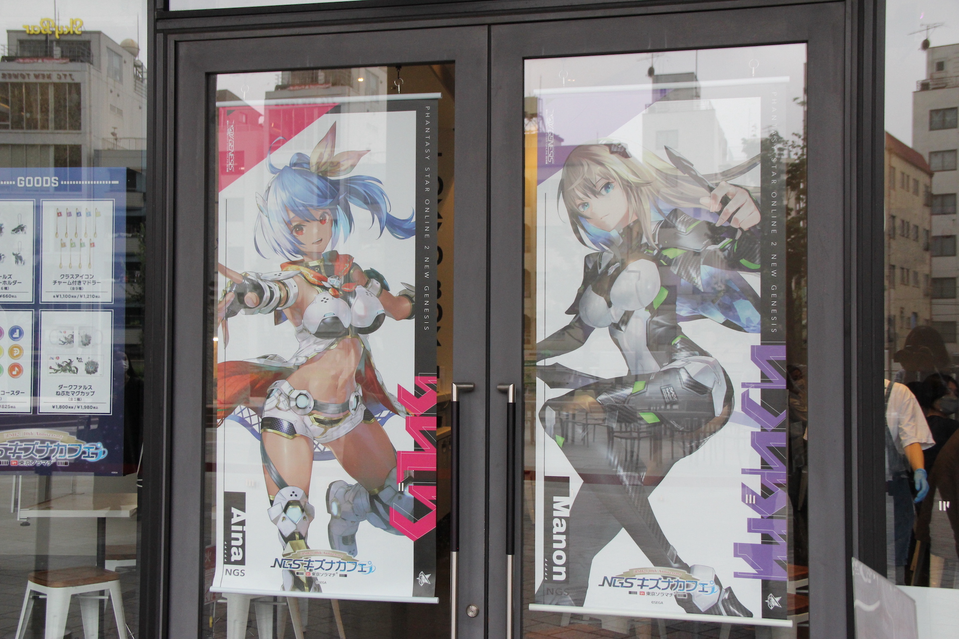 入り口の看板には、「NGSキズナカフェ」と大きく描かれているのが目立つ。窓には商品案内ポスターが張ってあるほか、ヒロインタペストリーも飾られている