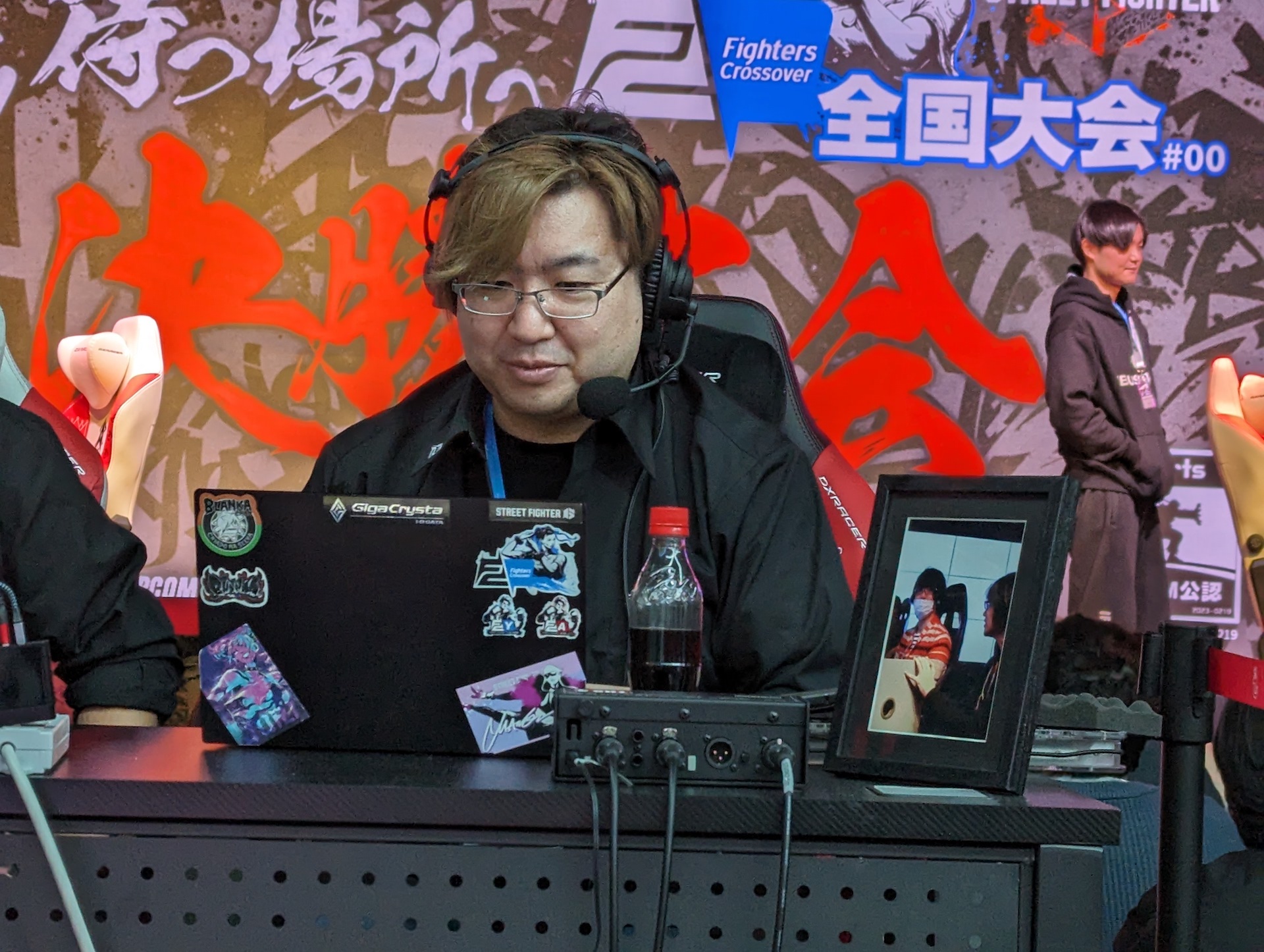 「Fighters Crossover」主催のかげっち氏。なお実況席でかげっち氏の横に置かれた写真は2023年7月に惜しくも他界したなない氏のもので、同氏もFighters Crossover出身の実況解説者だ