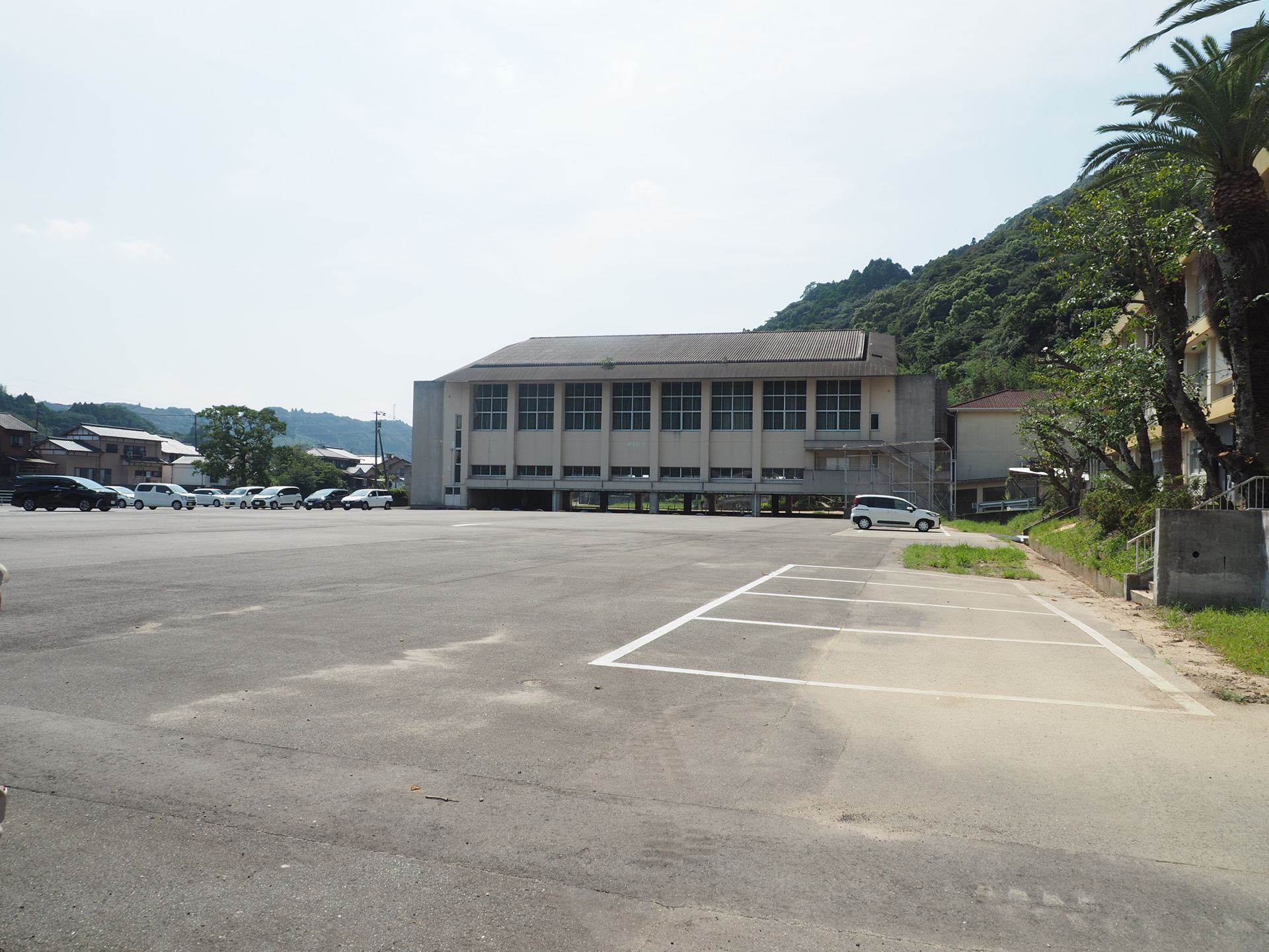 校庭は砂だったが、アスファルトが敷かれ駐車場として活用されている。奥の建物は体育館だが、こちらは使われていない