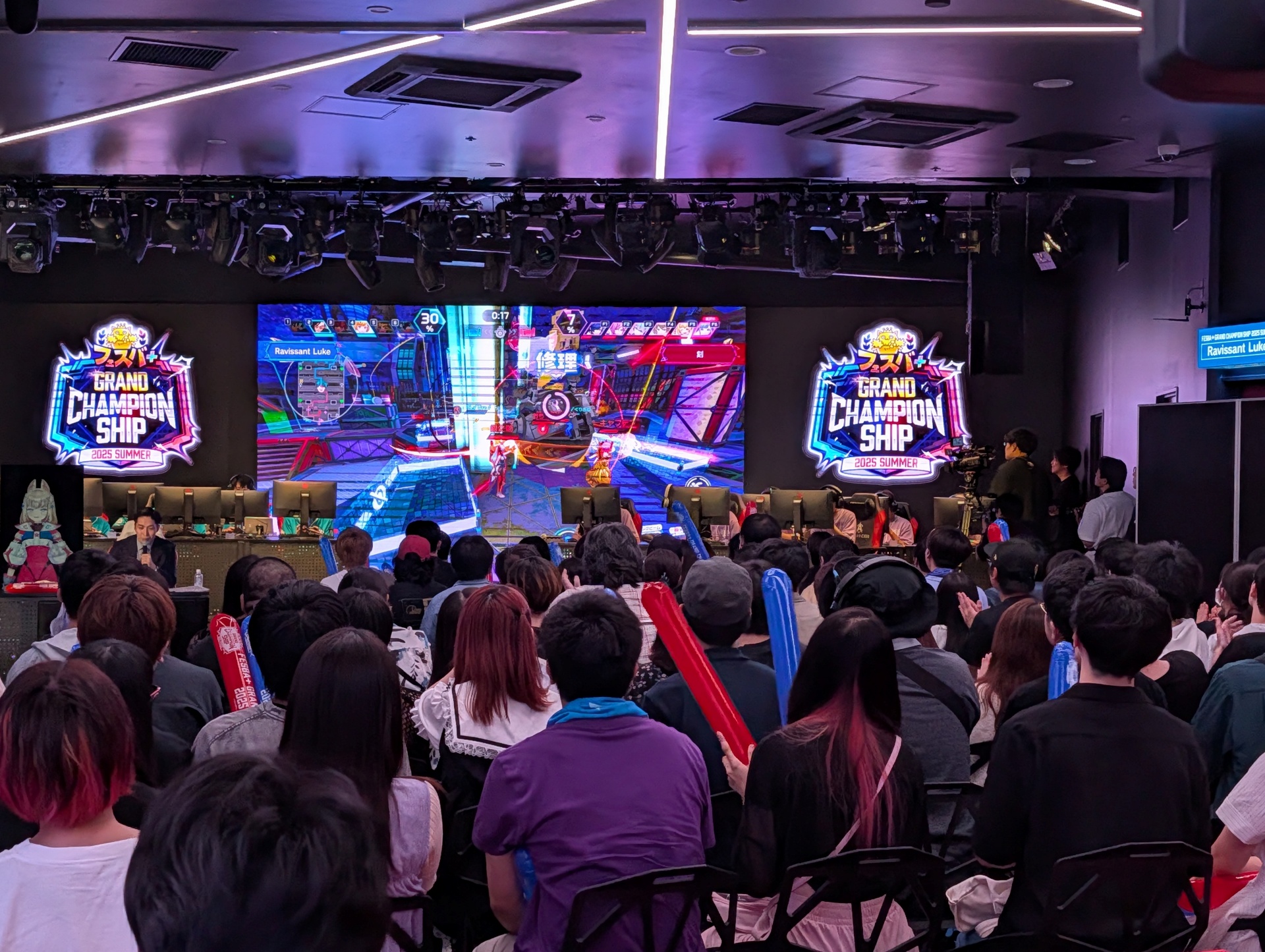 試合中のステージの様子。ゲーム内の様子を表示するステージの大型ディスプレイの下部に机が被さっており、やや見えにくい
