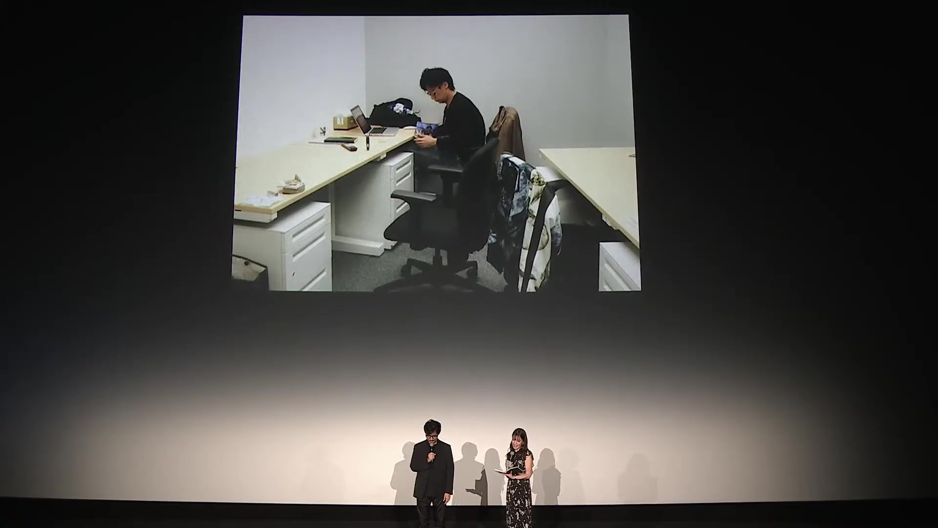 四畳半のオフィスで1人作業をする小島監督