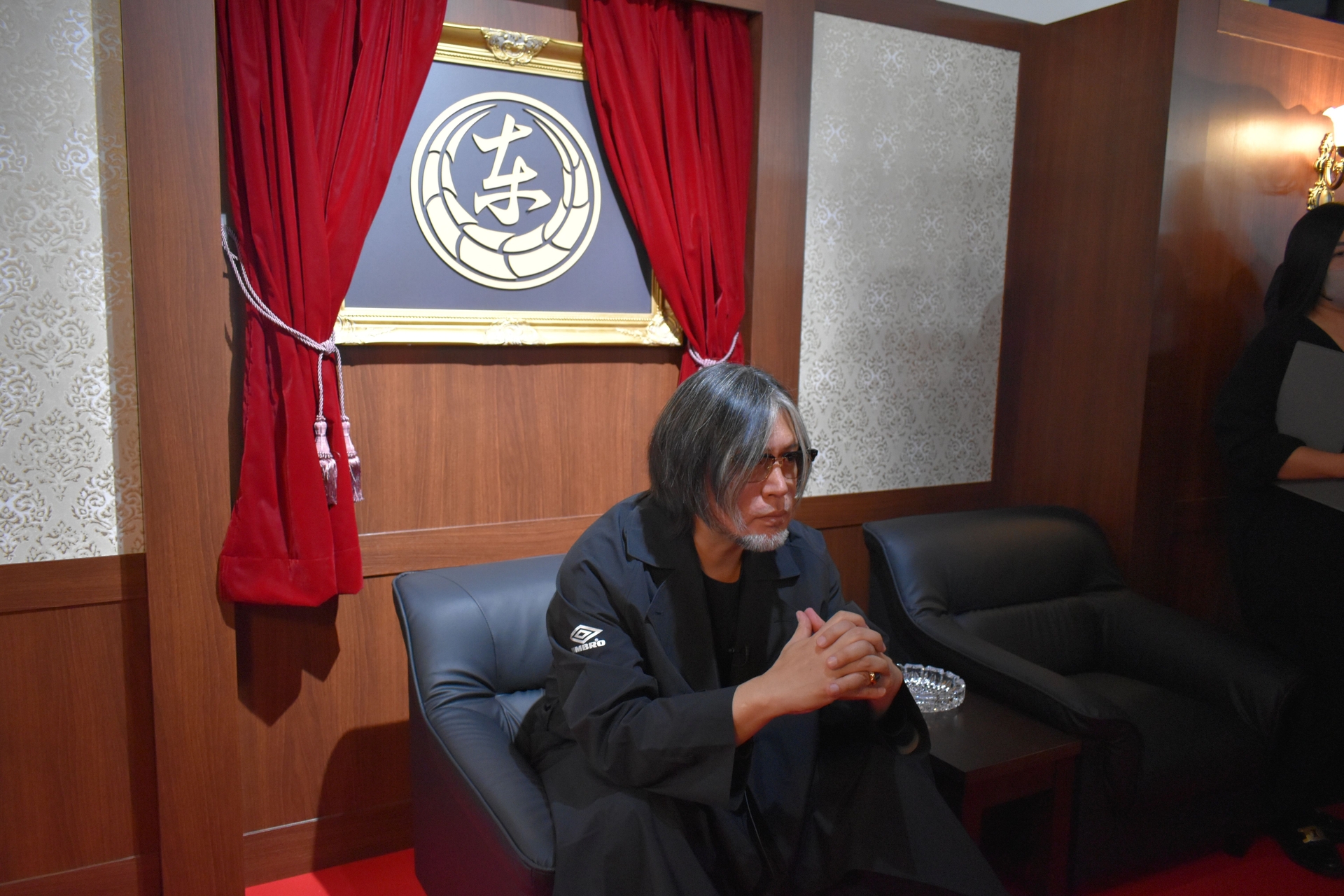 東城会の代紋をバックにポーズを決める横山氏