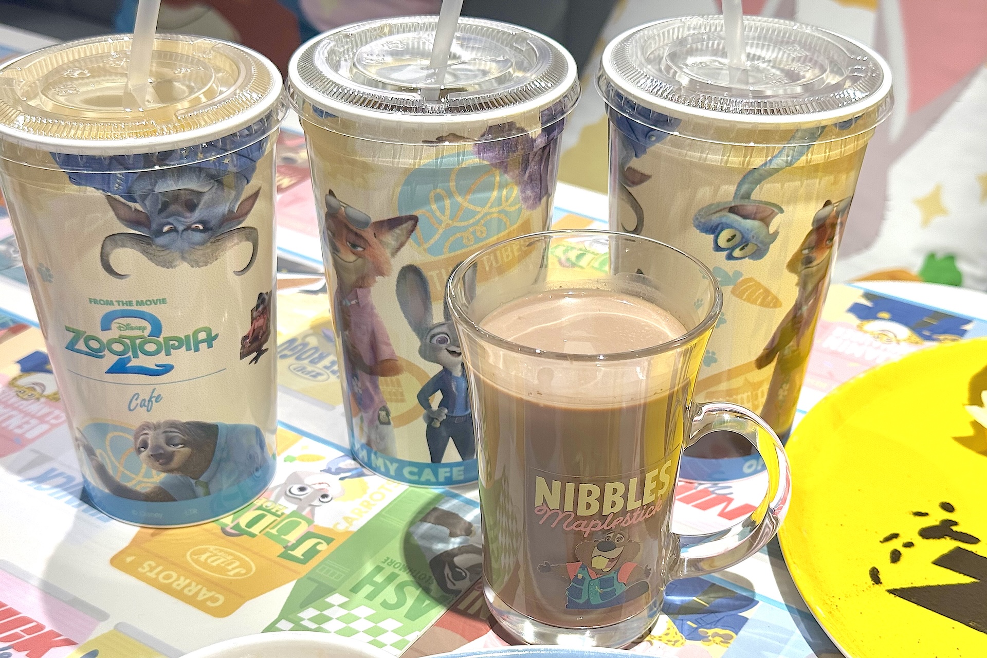 オリジナルリユースカップで提供されるのはオレンジジュース、アイスコーヒー、アイスティー 各990円。テイクアウト可能。手前のドリンクは＜ニブルズ＞ホットココア 990円。それぞれ特典コースター付き