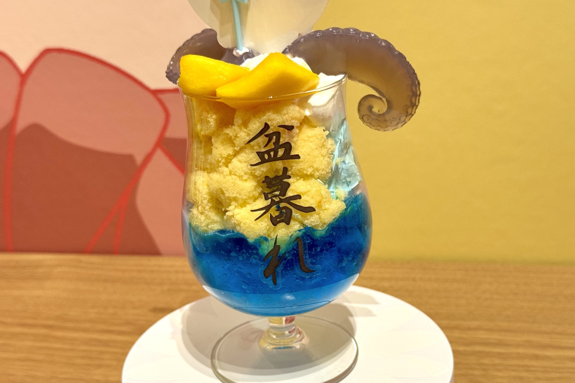 タコパフェはなんと回転する台座に乗った状態で提供される。パフェグラスの裏側には渋い書体で「盆暮れ」の文字。演出が細かい！