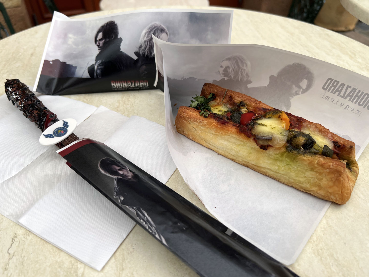 左が「レオン・S・ケネディのビターチョコレート・チュリトス」、右が「グリーンハーブの回復クロワッサンドッグ」。包み紙にもレオンとグレースがいる