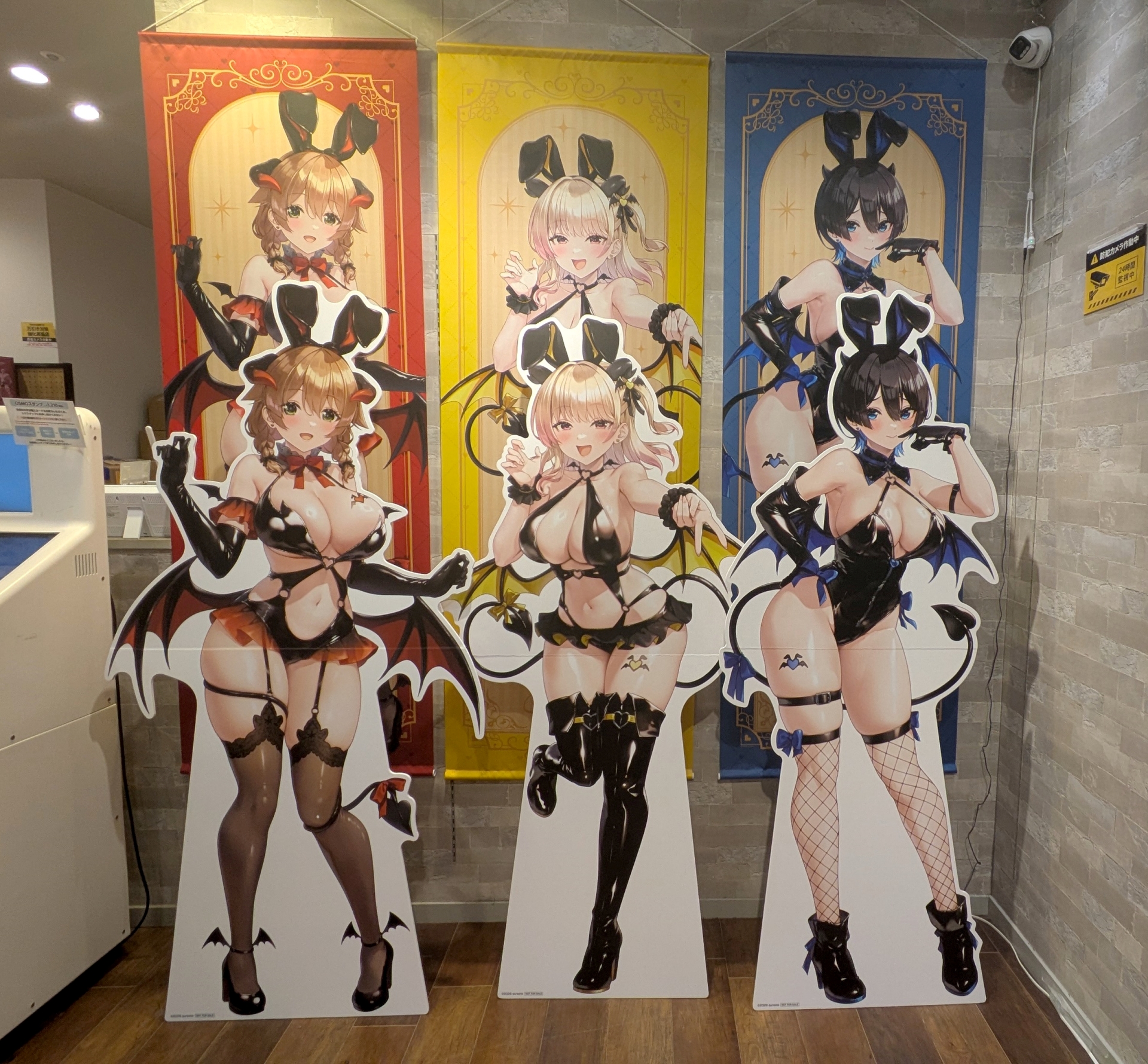 3人並んだ等身大パネル。衣装のデザインがそれぞれ微妙に異なるが、全員凄まじいボディである。背後に飾られているのが「等身大タペストリー（各9,900円）」で、サイズだけでいえば等身大パネルより更に大きい