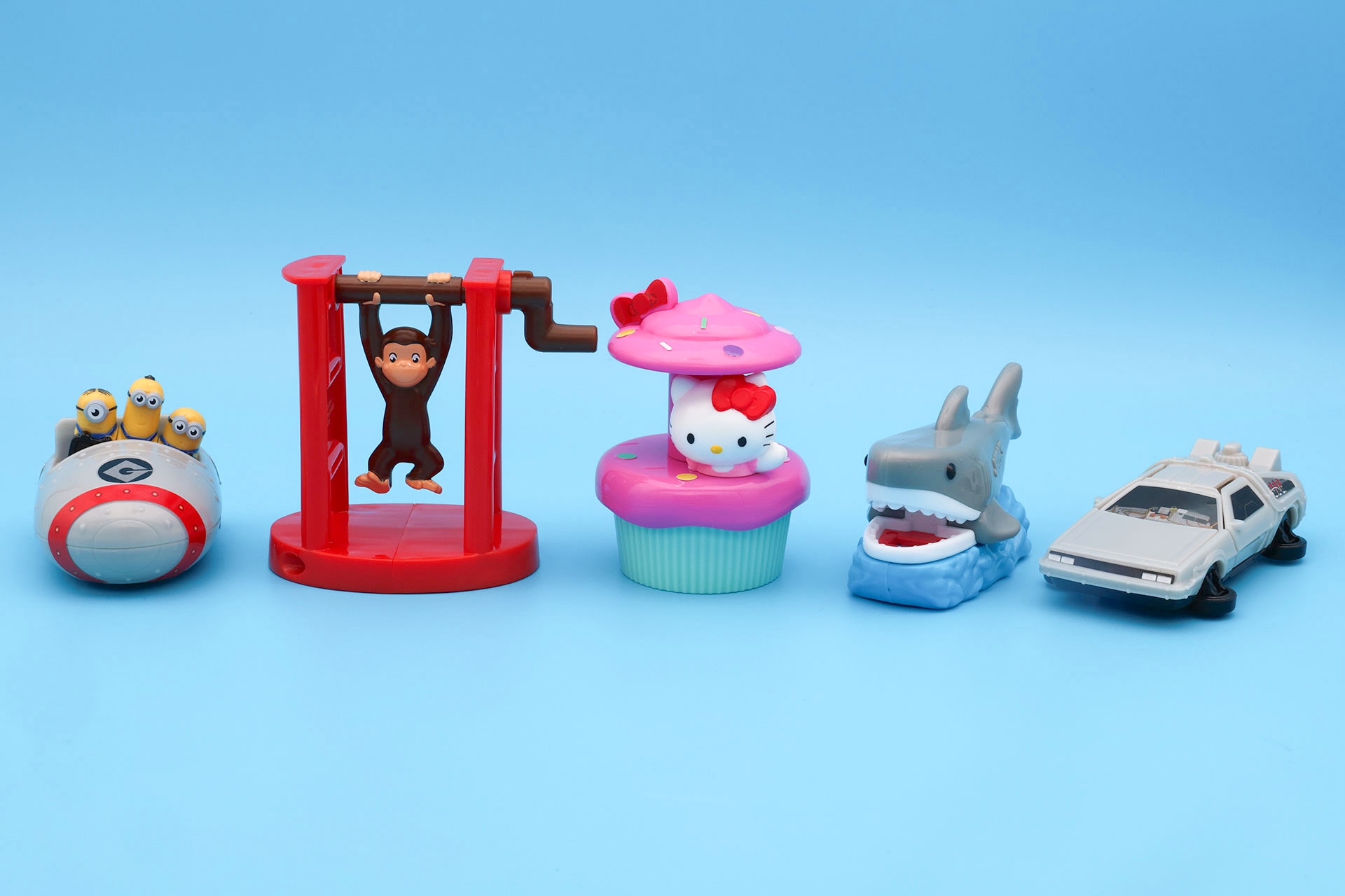 こちらが第1弾（10月16日〜10月22日）のハッピーセット「USJオールスターズ」に登場するおもちゃ。写真左から「ミニオン・ハチャメチャ・ライド ゆらゆらカー」、「プレイング・ウィズ おさるのジョージ」、「ハローキティのカップケーキ・ドリーム 小物入れ」、「ジョーズの歯形スタンプ」、「バック・トゥ・ザ・フューチャー ダブルドアカー」