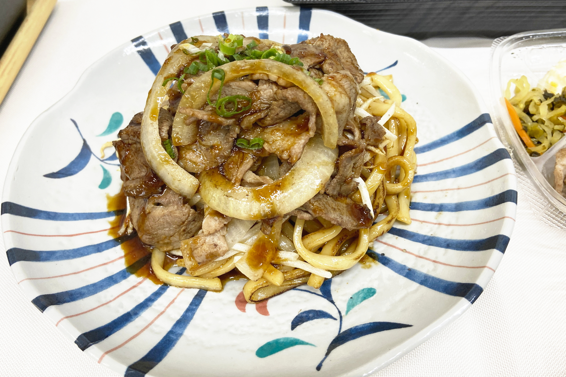 おすすめアレンジレシピ「ラムジンギスカンうどん」。おかずのみの「ラムジンギスカン」を購入し、炒めたうどんの上に盛り付ける