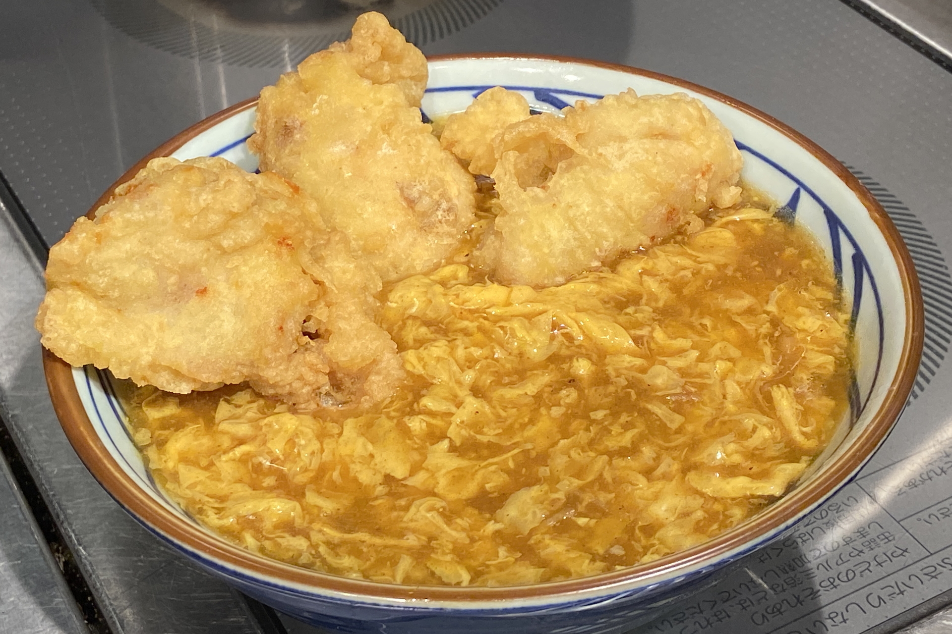 京風のカレーあんかけをベンチマークにしたカレーうどんの上に、塩胡椒とカレー粉で味つけした鶏天を3つ、カレー味のそぼろ、無塩バターをトッピング