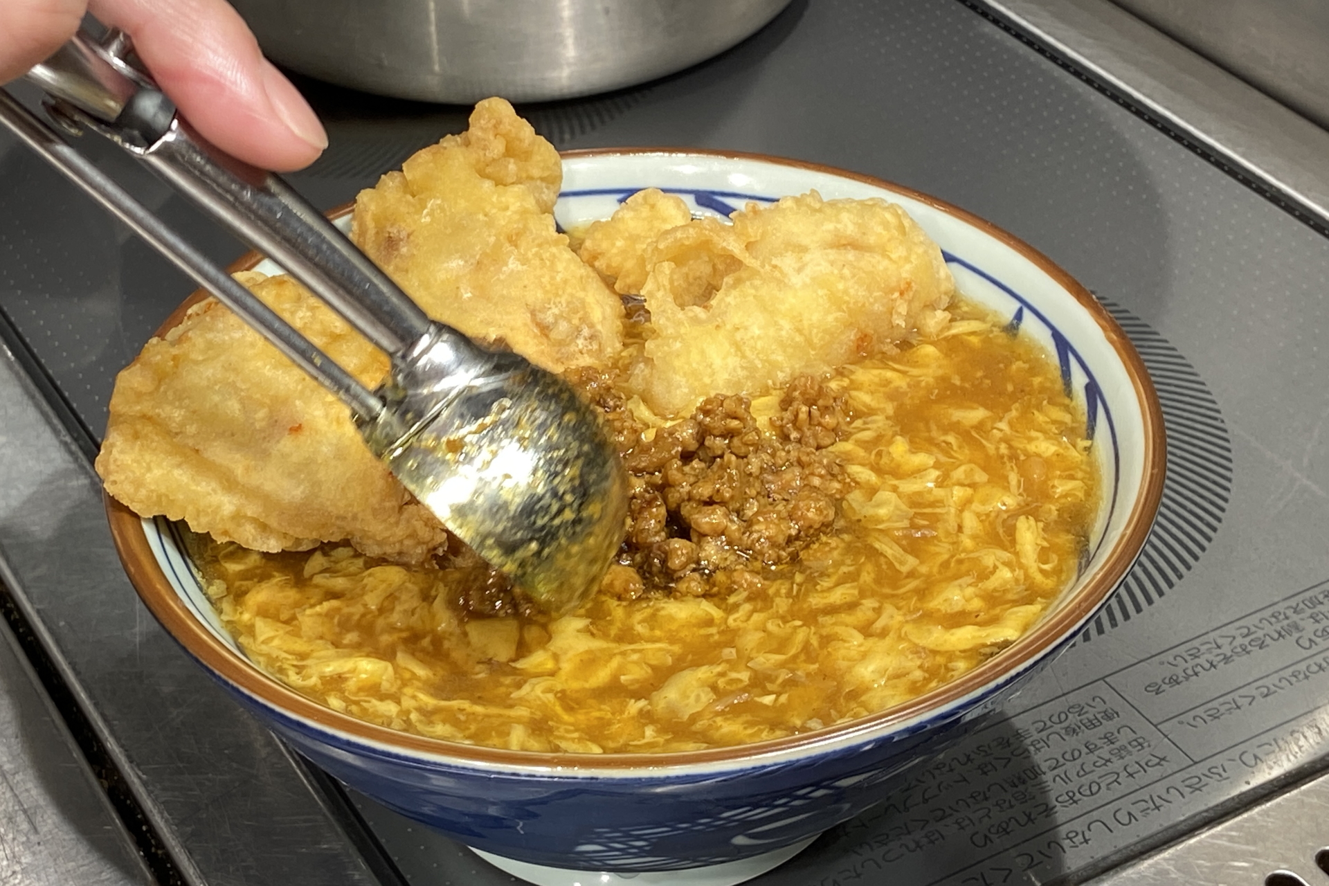 京風のカレーあんかけをベンチマークにしたカレーうどんの上に、塩胡椒とカレー粉で味つけした鶏天を3つ、カレー味のそぼろ、無塩バターをトッピング