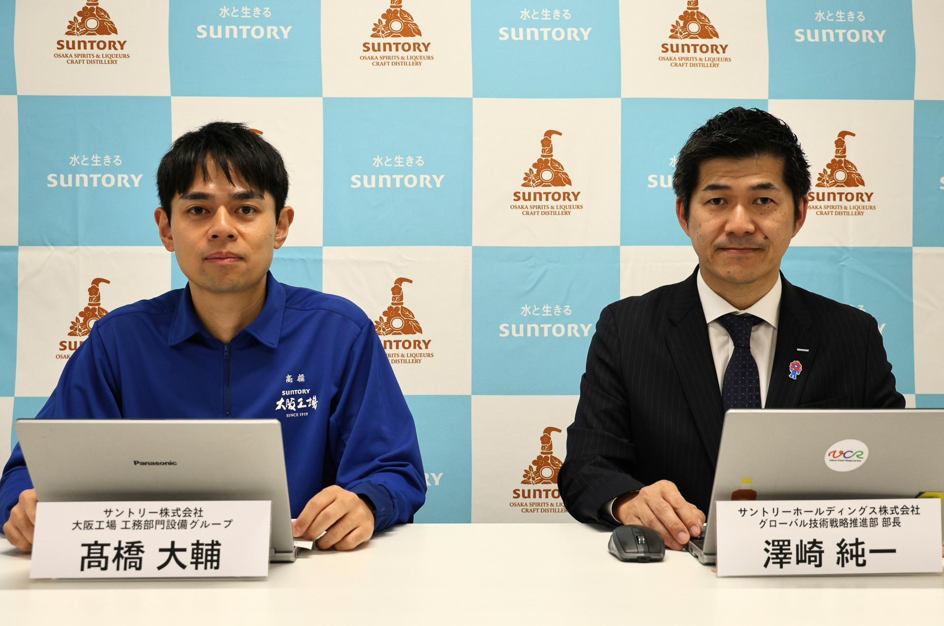 大阪工場「スピリッツ・リキュール工房」のハンドリング自動化を説明した（右から）サントリーホールディングス株式会社 グローバル技術戦略推進部 部長 澤崎純一氏とサントリー株式会社 大阪工場 工務部門設備グループ 高橋大輔氏