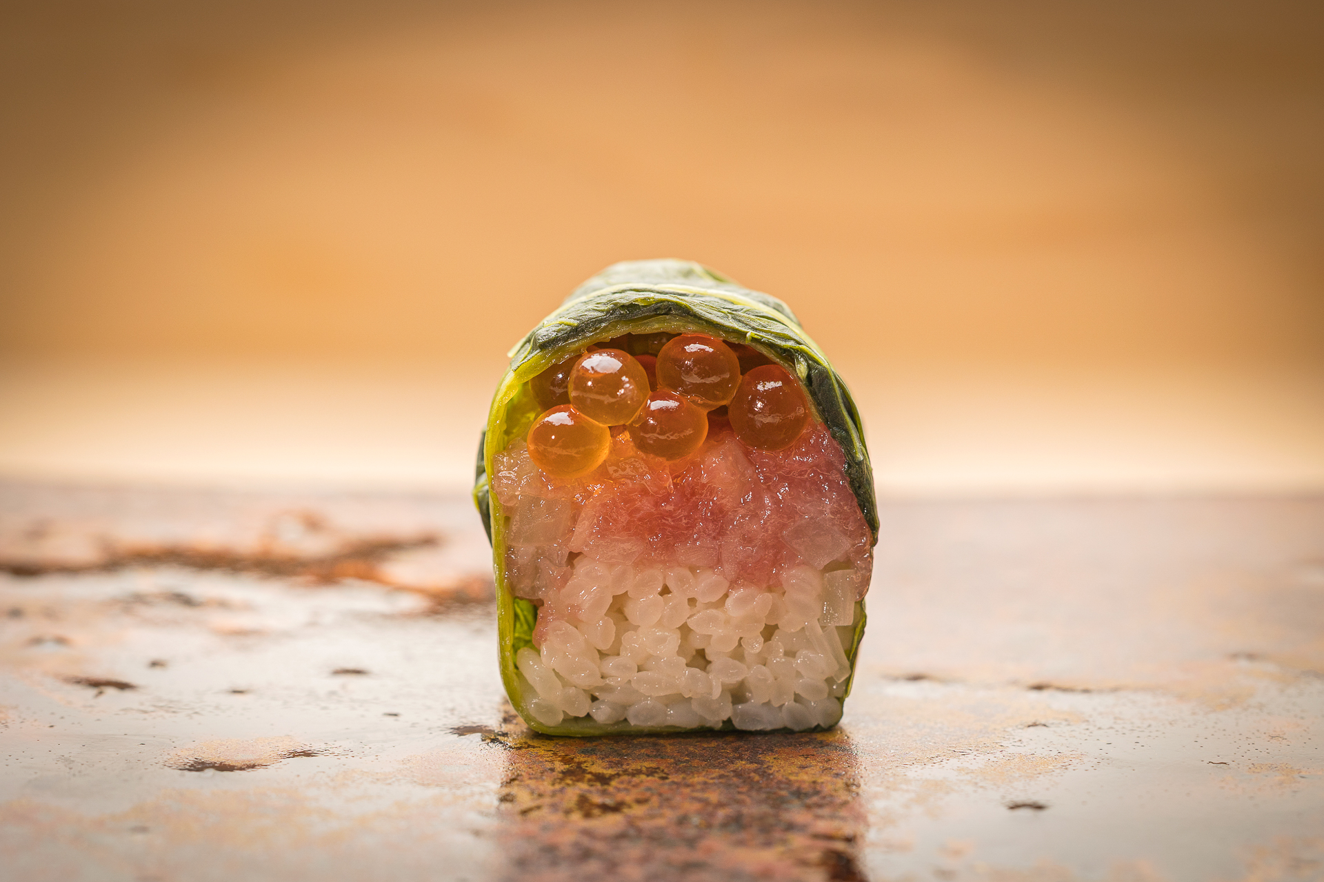 和歌山の郷土料理「目張寿司」をアレンジ。刻んだ鮪トロ、らっきょう、いくらと酢飯を層状に重ねて高菜の葉で包んでいる