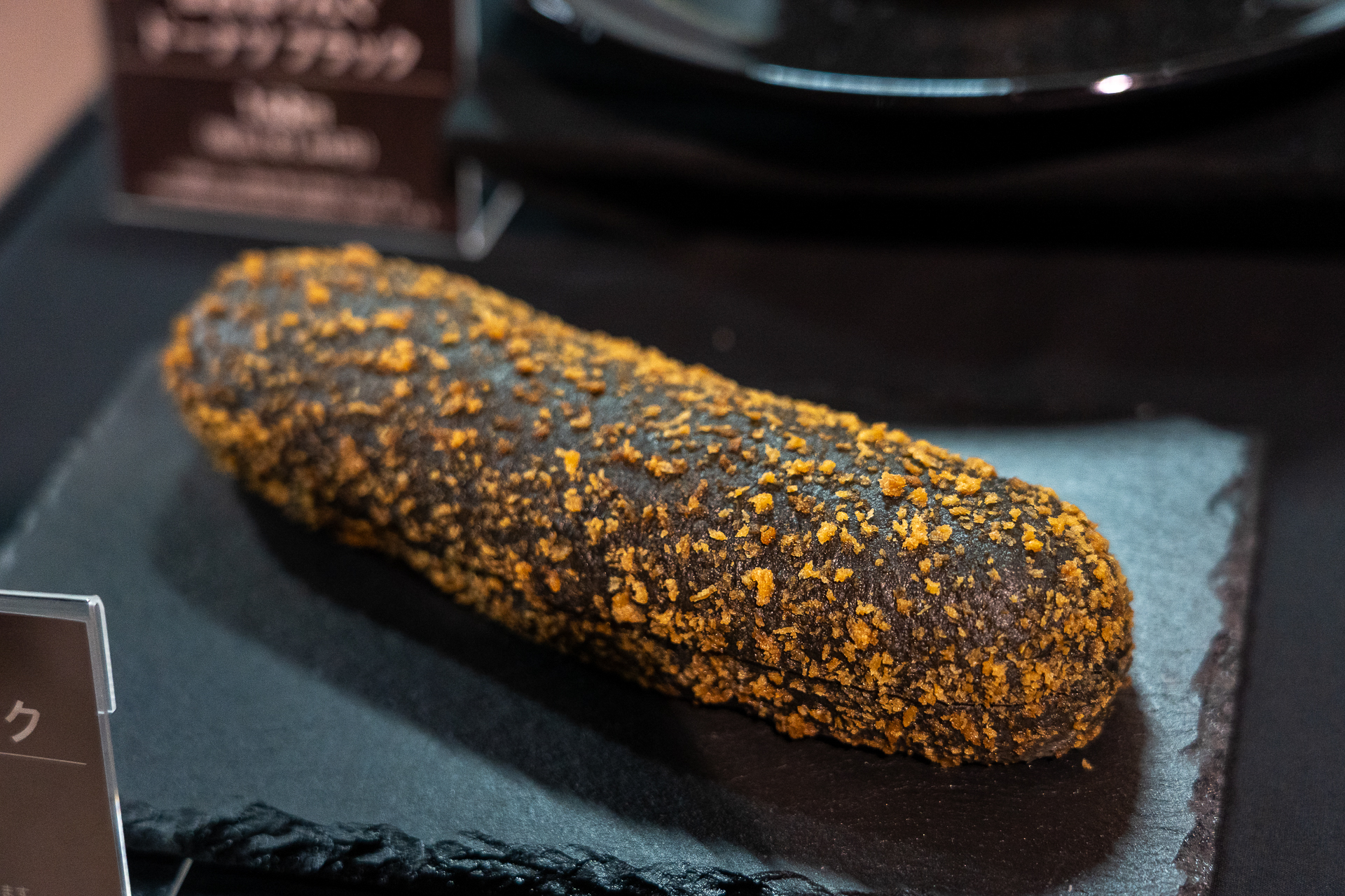 カレー棒 ブラック。黒い生地に鮮やかなオレンジのパン粉をまぶした惣菜パン