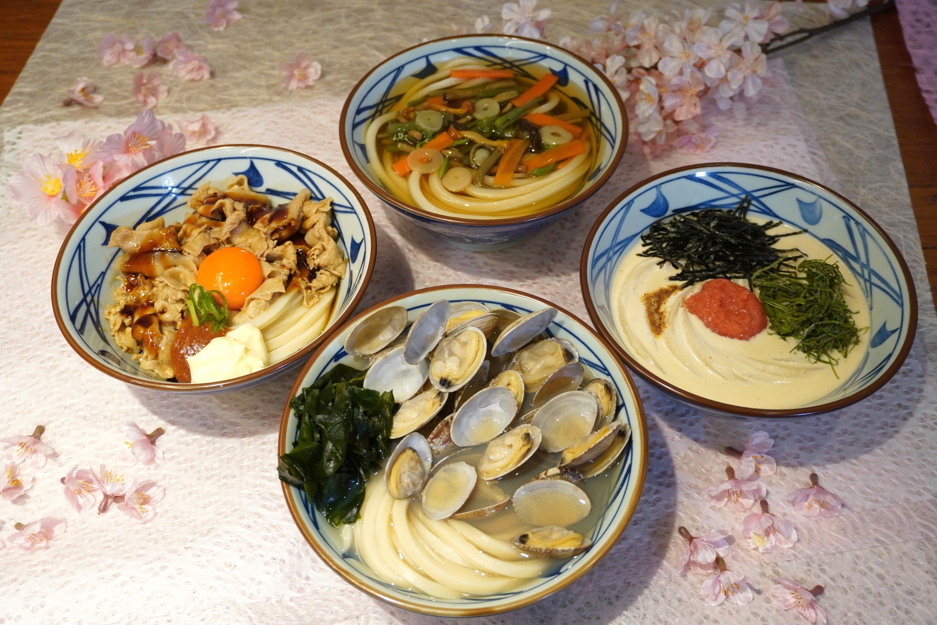 丸亀製麺の（手前から時計回りに）「山盛りあさりうどん」「こく旨 豚玉ぶっかけうどん」「山菜うどん」「明太クリームうどん」