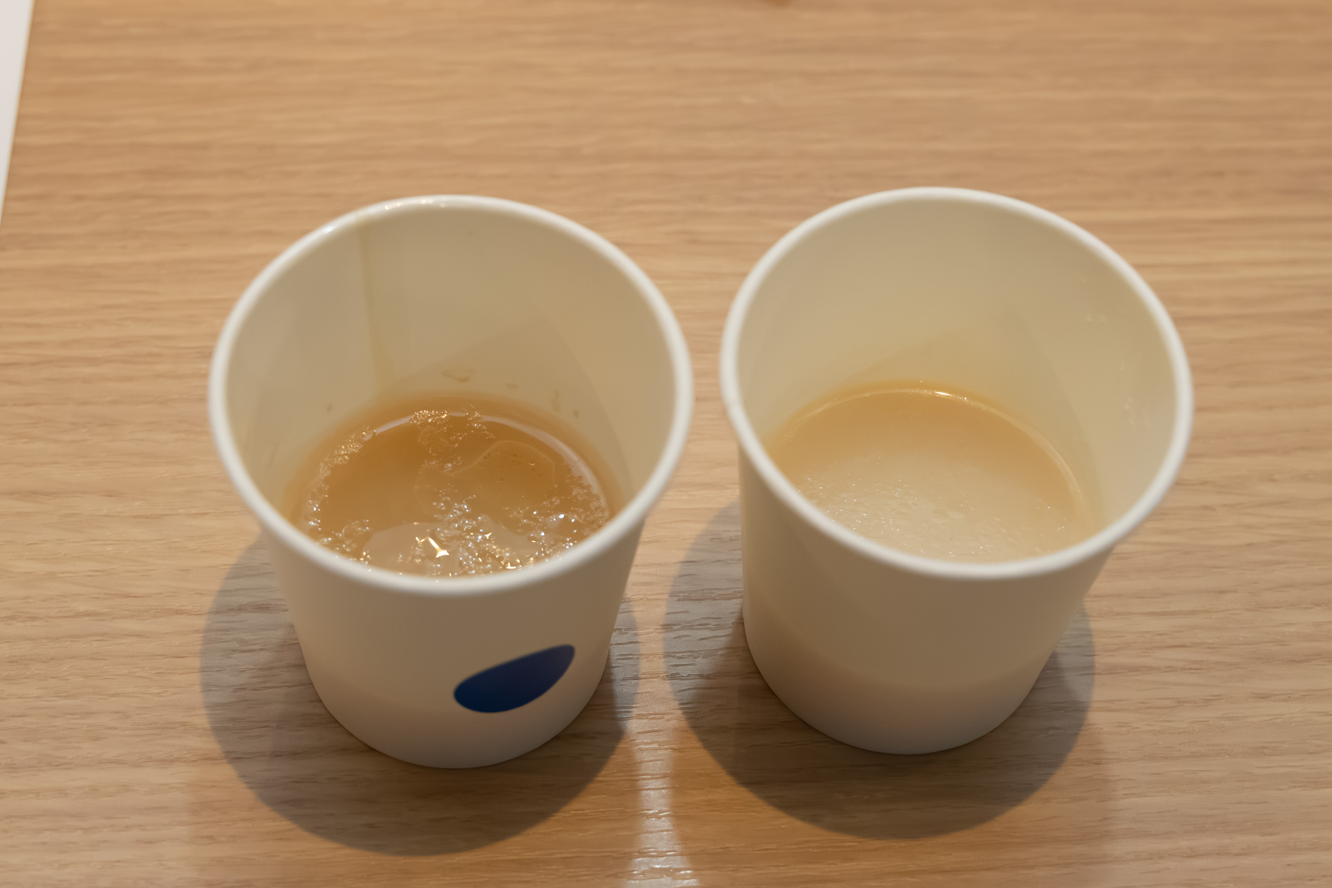 レギュラーの「とんこつラーメン」と「濃厚豚骨醤油ラーメン」（青いシール）のスープも比較用に提供された。表面の油膜の厚さからも濃厚さが伝わってくる