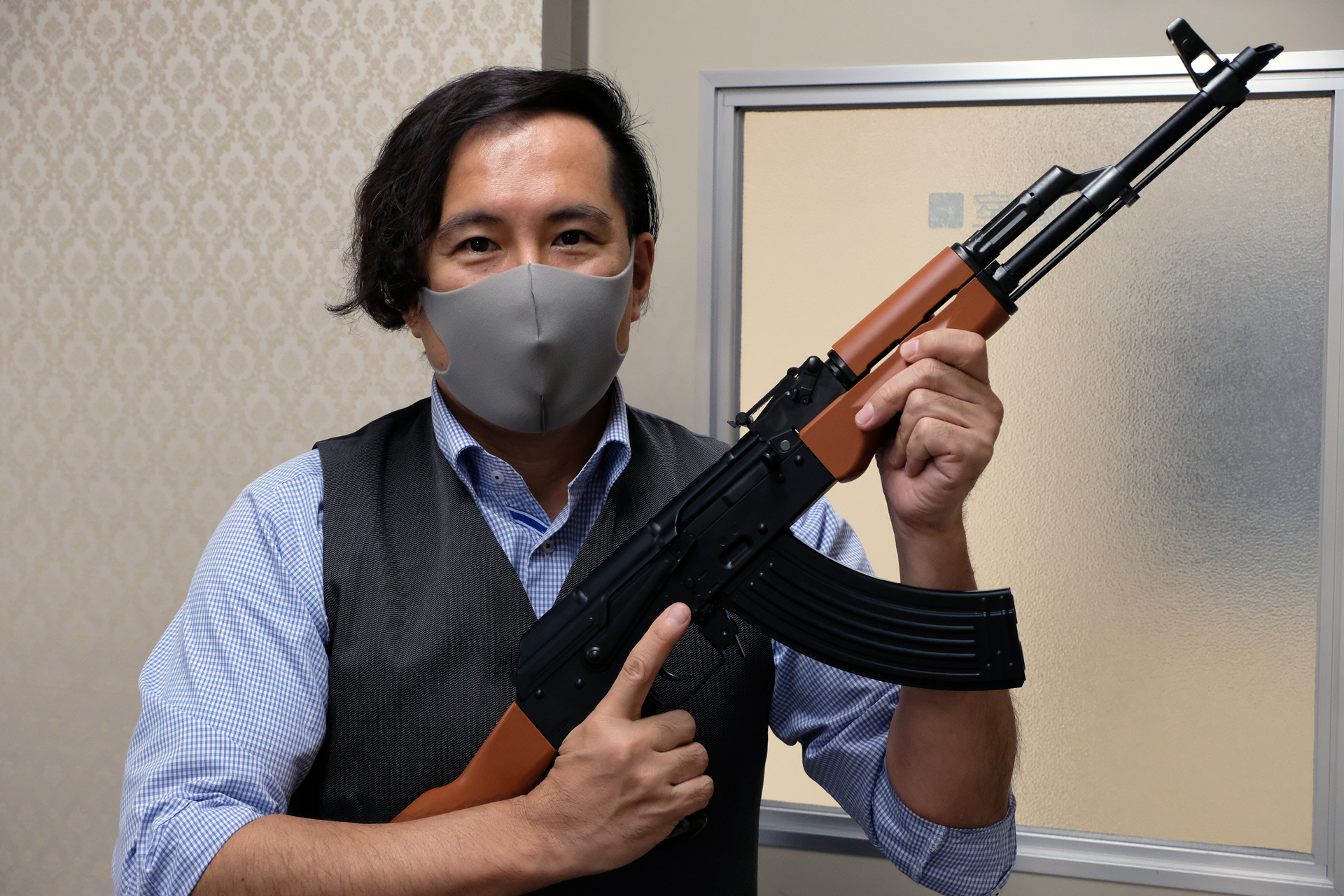 「ガスブローバックマシンガン AKM」を構える東京マルイの広報を務める島村優氏。軍服だけでなく、背広や民族衣装など、どんな服でも似合うのがAKの大きな魅力と言える