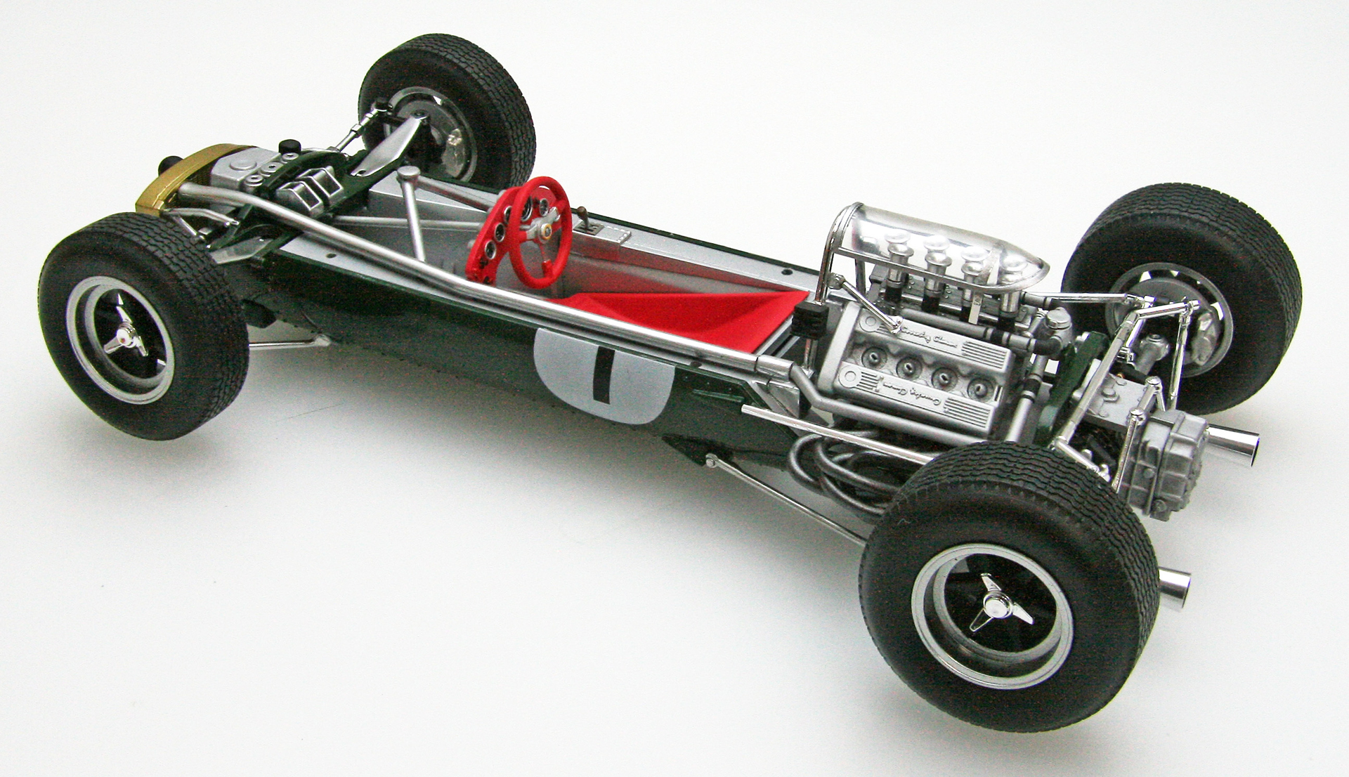 エブロが「1/20 ロータス33」用に作り起こしたエッチングパーツと、アルミの挽物で製作したエンジンのエアファンネル＆メガフォンタイプのエキゾーストテールパイプ（と、それらを埋め込んだ「ロータス33」の完成見本画像）。エアファンネルなどはプラスチックで成型するとパーティングライン（※プラスチックパーツ成形時に生じる接合線）が生じてしまいその接合線を紙ヤスリで消して銀色に塗装して……という手間を考えると大変面倒臭いためアルミの挽物パーツを付属させてくれると大変助かるのだが、その半面、金属パーツを付属させると商品価格が高騰してしまうためモデルメーカーとしては非常に悩みどころになる。言ってしまえばエブロ＝木谷氏は「どうせこの『ロータス33』を買ってくれるのは相当なF1マニアなのだから」と割り切った上で、価格の高騰化を見据えた上で「とにかく格好よく仕上がる『ロータス33』」を目指したということなのだろう