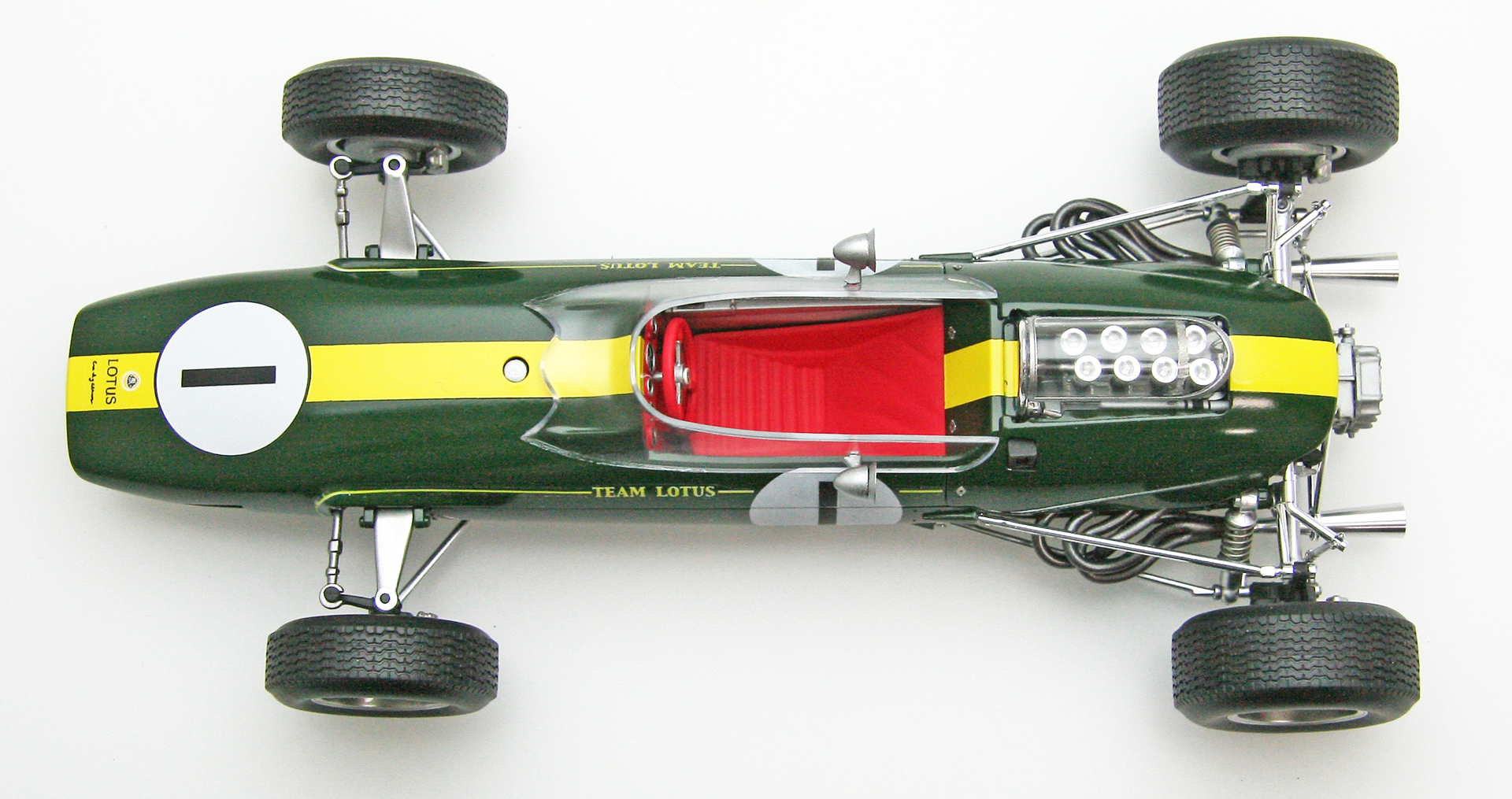 エブロが「1/20 ロータス33」用に作り起こしたエッチングパーツと、アルミの挽物で製作したエンジンのエアファンネル＆メガフォンタイプのエキゾーストテールパイプ（と、それらを埋め込んだ「ロータス33」の完成見本画像）。エアファンネルなどはプラスチックで成型するとパーティングライン（※プラスチックパーツ成形時に生じる接合線）が生じてしまいその接合線を紙ヤスリで消して銀色に塗装して……という手間を考えると大変面倒臭いためアルミの挽物パーツを付属させてくれると大変助かるのだが、その半面、金属パーツを付属させると商品価格が高騰してしまうためモデルメーカーとしては非常に悩みどころになる。言ってしまえばエブロ＝木谷氏は「どうせこの『ロータス33』を買ってくれるのは相当なF1マニアなのだから」と割り切った上で、価格の高騰化を見据えた上で「とにかく格好よく仕上がる『ロータス33』」を目指したということなのだろう