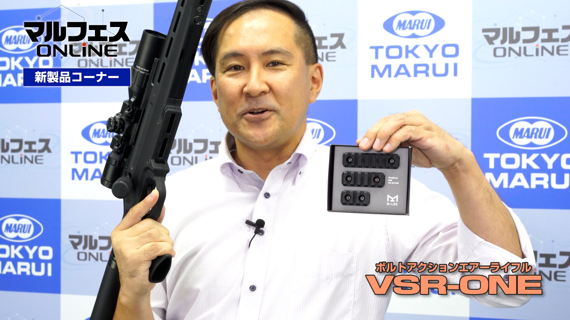 マルフェスオンラインの発表時、Mロックと「VSR-ONE」を持つ島村広報。心なしかいつもより嬉しそうに見える