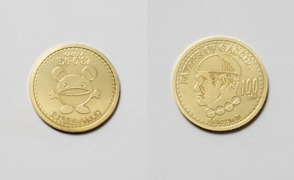 表はガチャ万博公式キャラクター「カプセルあけまくる君」/裏は近代ガチャの父、G.G.ローリング3世