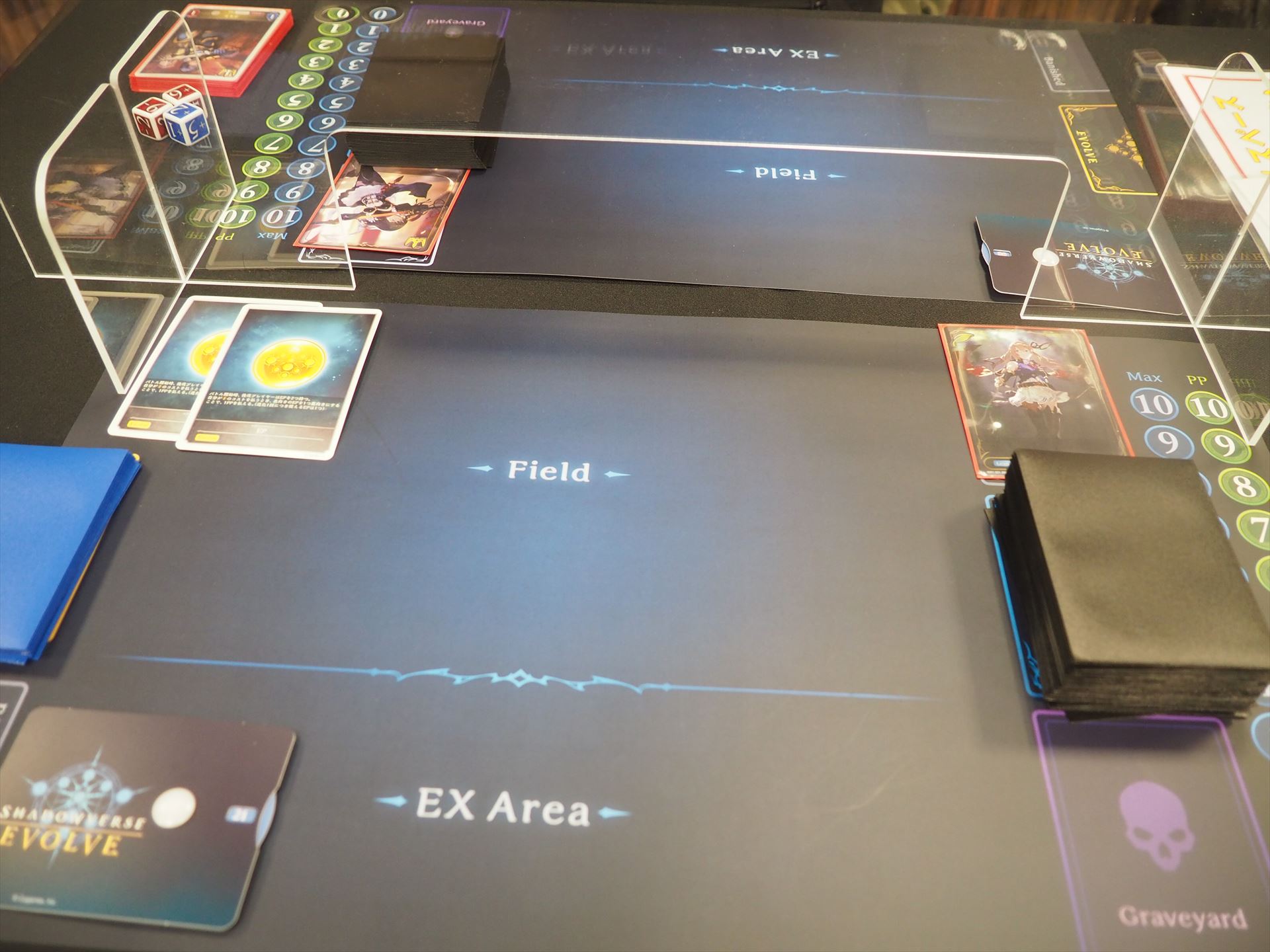 「Shadowverse EVOLVE」のフィールド。手前が手札の拡張として使える「EXエリア」、その奥が「フィールド」、右上には「リーダーカード」を置き、その下がデッキ、その下が墓場となる。一番右側にはMaxとPPを示すカウンターがある。左の青いスリーブはエボルヴデッキである。左上に並んでいるのは「エボルヴポイントカード」であり、後攻プレーヤーが2枚持てる