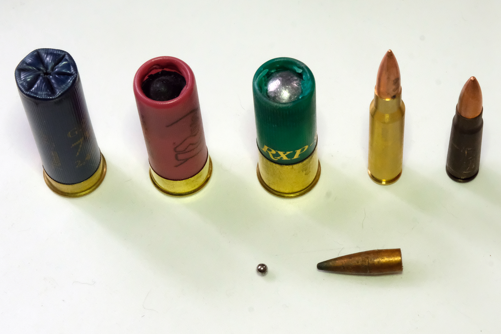 ダミーカート画像。後列左3つがショットガンのショットシェル。真ん中の緑色のショットシェルの先端に大きな散弾が見える。右側2つがライフル弾。前列左が球状の小粒散弾、右はライフル弾の流線型の弾頭