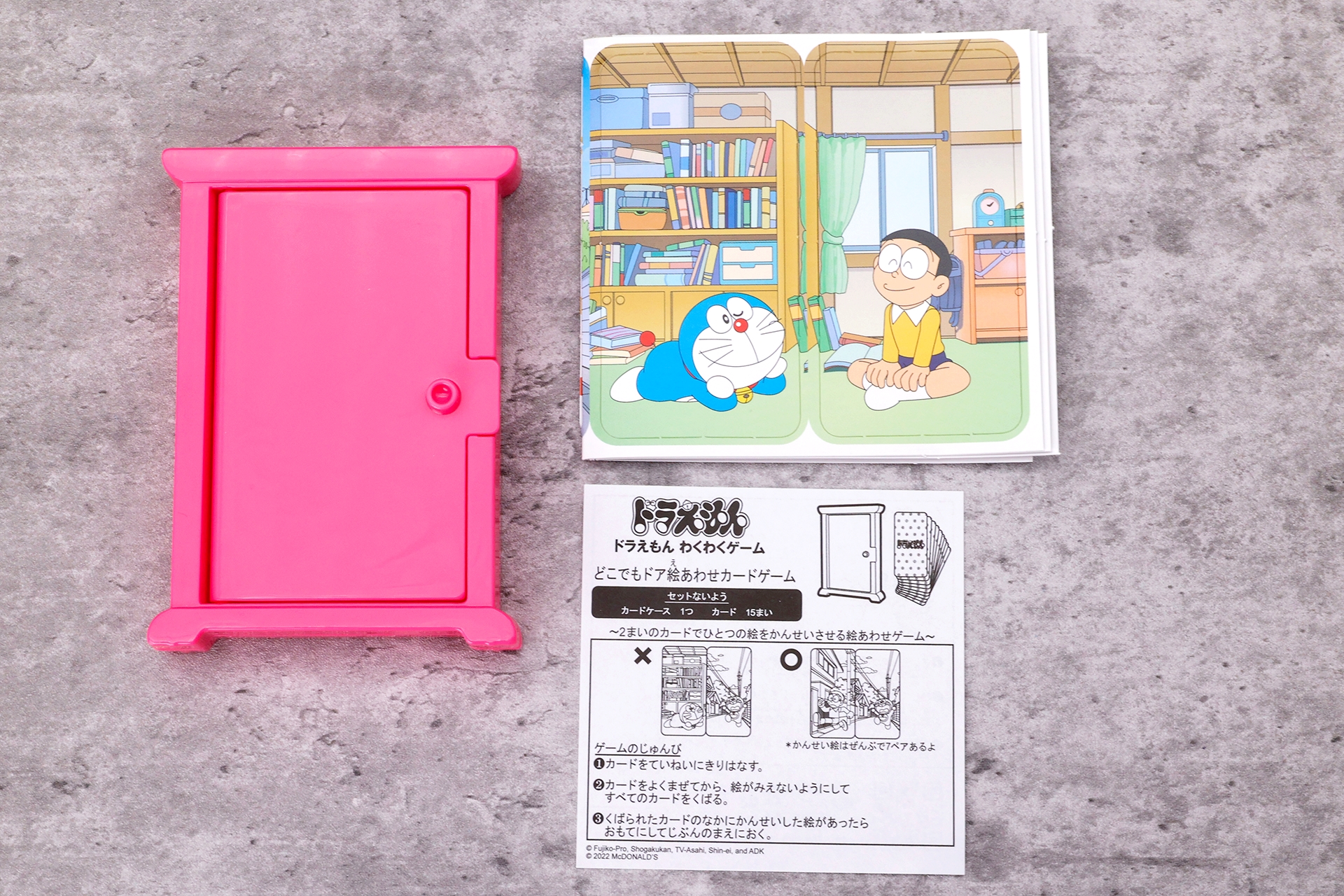 こちらが「どこでもドア絵あわせカードゲーム」のおもちゃ袋の中身。どこでもドアの形をしたカードケースと、カードが15枚、説明書といった内容になっている