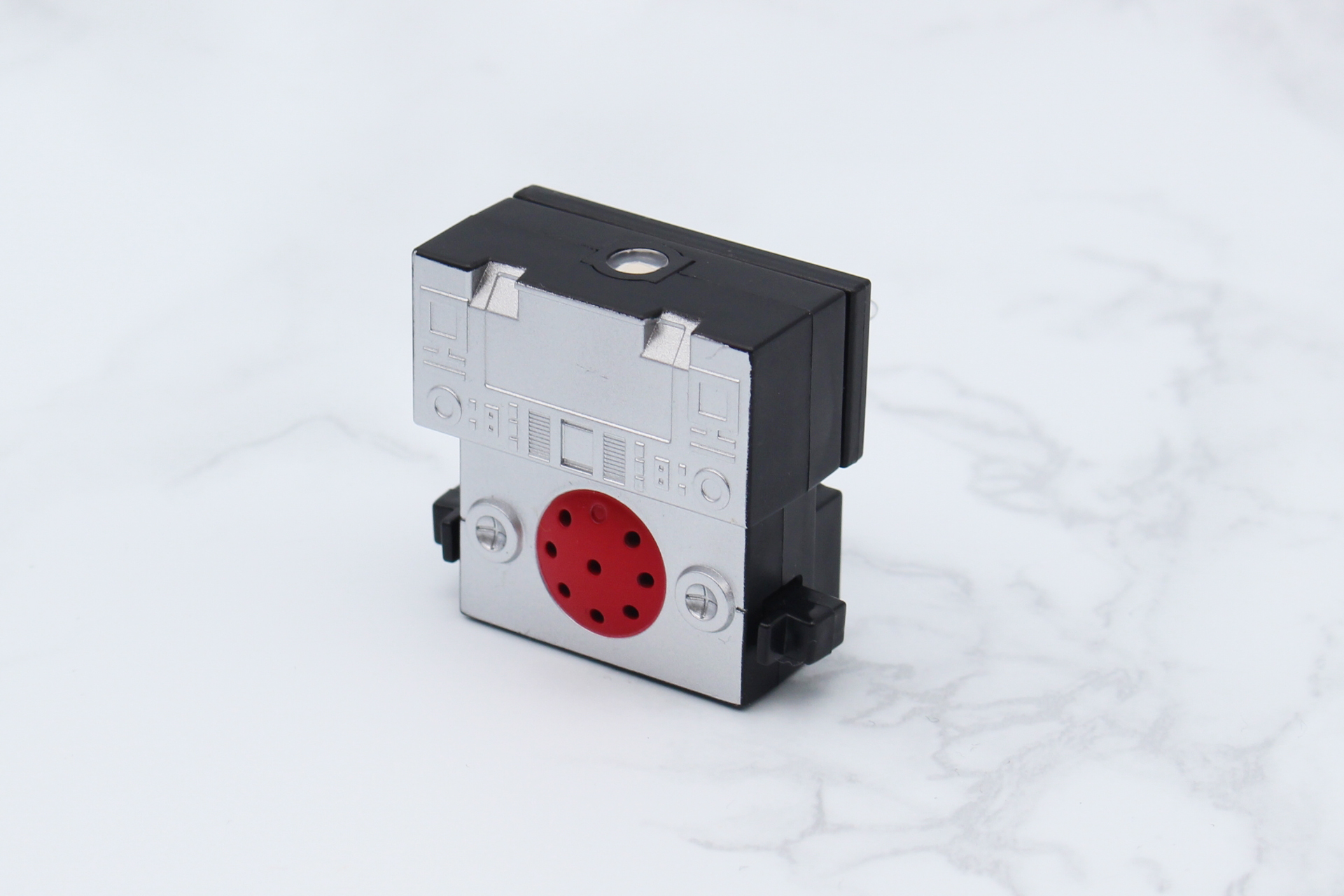 グラビトンユニット。赤い部分がスピーカー、その左右にボタン式スイッチ、上面にLEDがある。ボタン電池LR41×3で稼働し、テスト用電池が付属