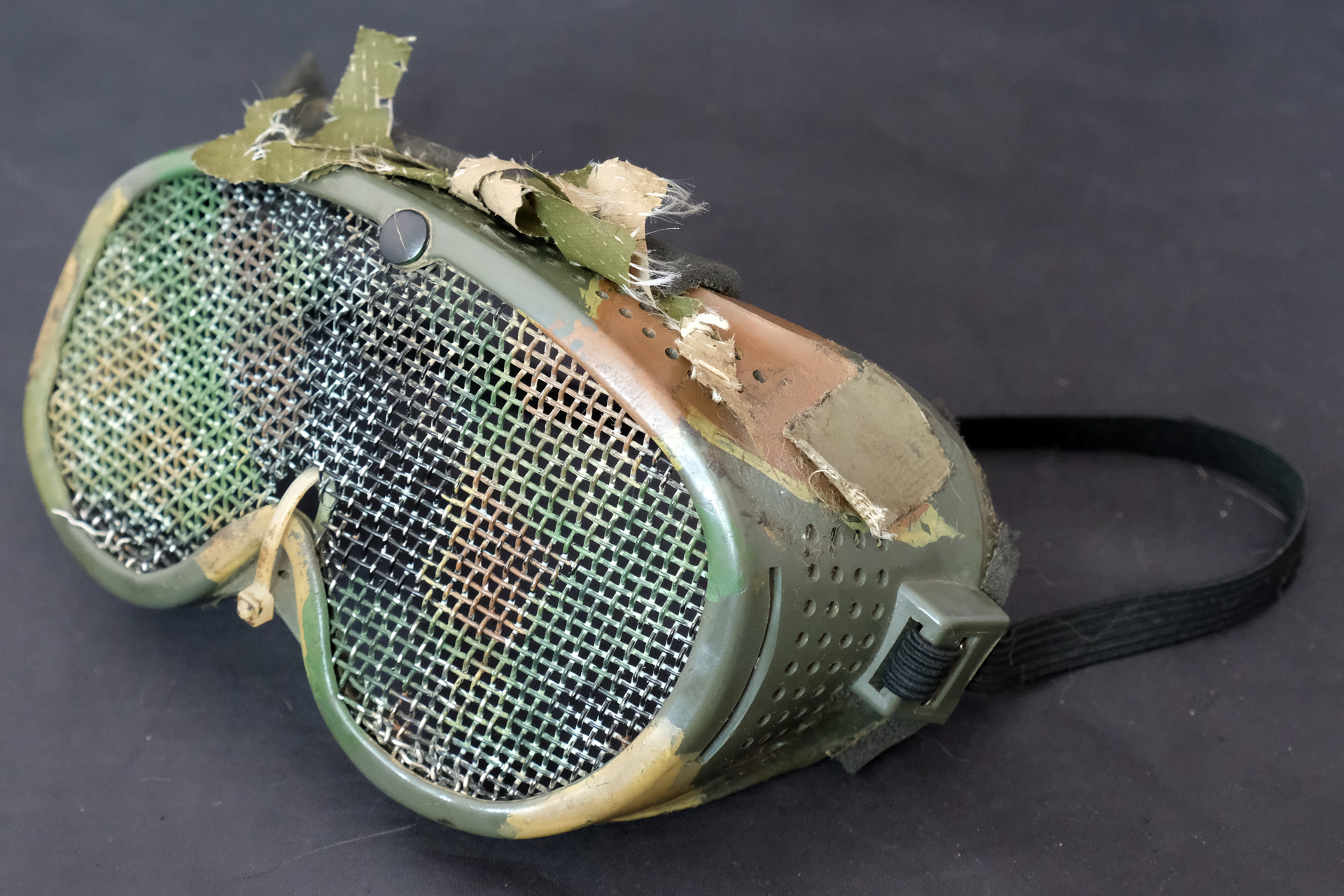 サンエイ「ゴーグル」、価格980円、1990年頃購入。レンズ部分を広田商事「メッシュ・シールド」価格680円に付け替え。1990年代から今も予備として愛用しているサンエイ（現サンセイ）のゴーグル。こちらも塗装と偽装網でカモフラージュを施してある