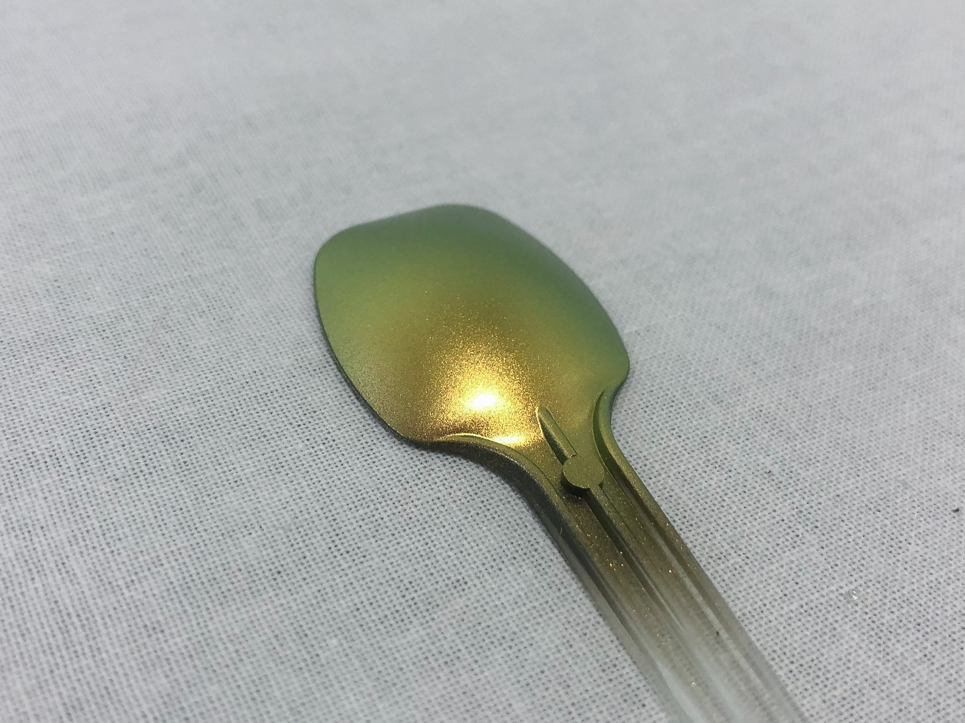 エアブラシで塗装したスプーンを斜め方向から見てみます。スプーンの縁がグリーンに偏光していることがわかります。