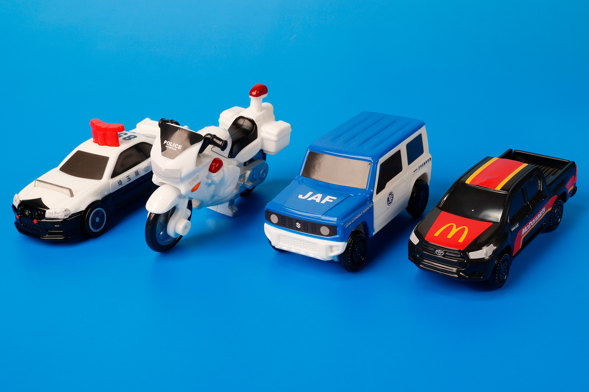 こちらが第1弾（4月14日～4月27日）のハッピーセット「トミカ」に登場するおもちゃ。写真左から「日産 スカイライン GT-R（BNR34）パトロールカー」、「Honda VFR 白バイ」、「スズキ ジムニー JAF ロードサービスカー」、「トヨタ ハイラックス」