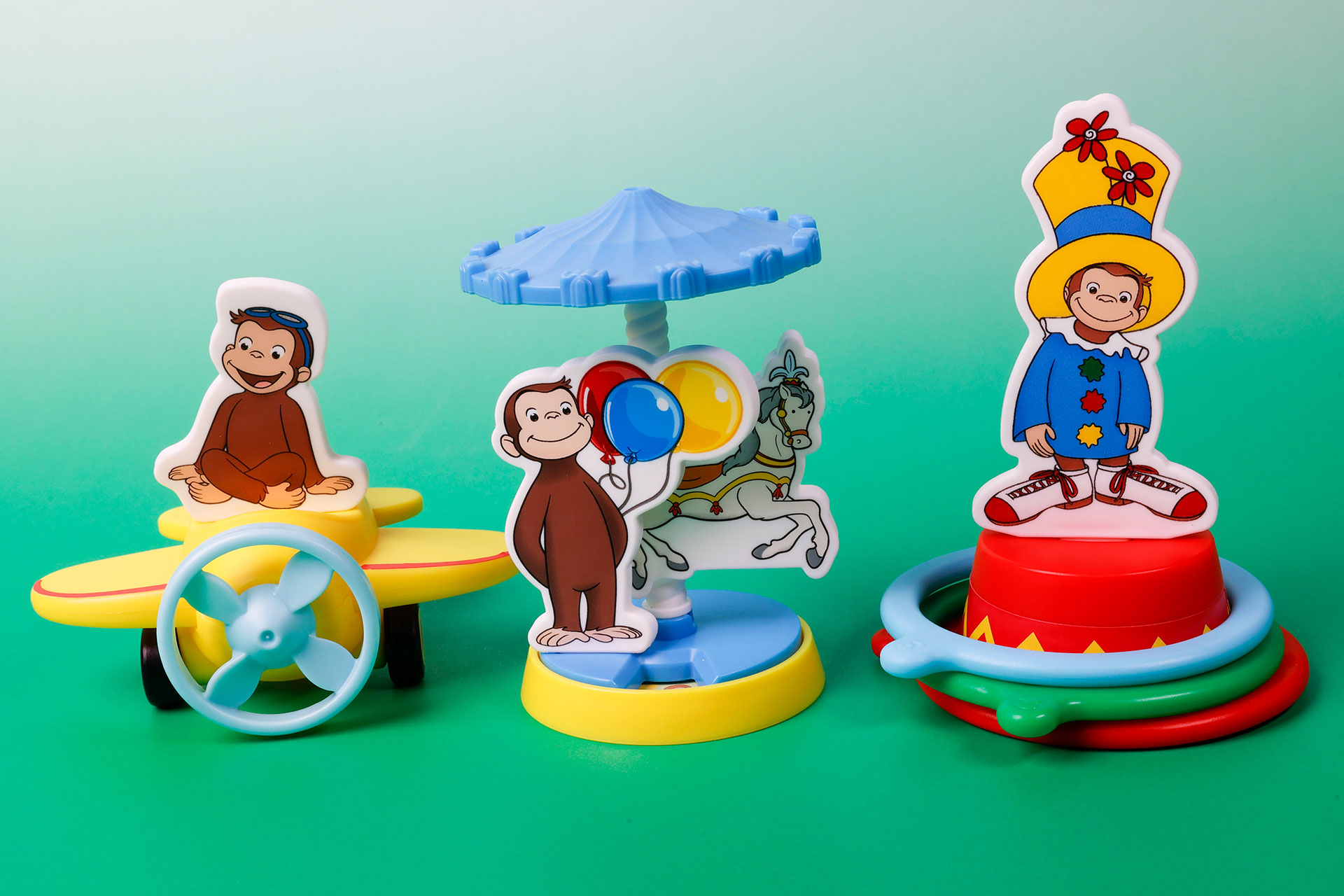 こちらが第2弾（6月23日～6月29日）のハッピーセット「おさるのジョージ」に登場するおもちゃ。写真左から「ジョージのひこうきライド」、「ジョージのぐるぐるゆうえんち」、「ジョージのカラフルわなげショー」