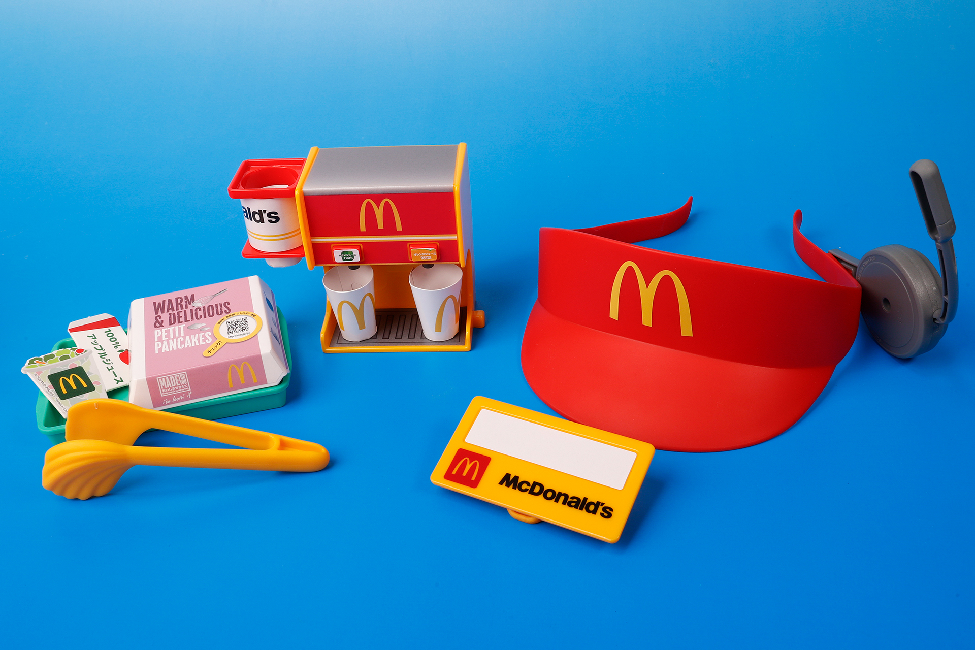 こちらが第2弾（7月21日～7月27日）のハッピーセット「マックアドベンチャー なりきりマクドナルド」に登場するおもちゃ。写真左から「つくってみよう！プチパンケーキセット」、「カップをとりだせる！ドリンクマシーン」、「クルーになりきろう！サンバイザー＆ネームバッジ」