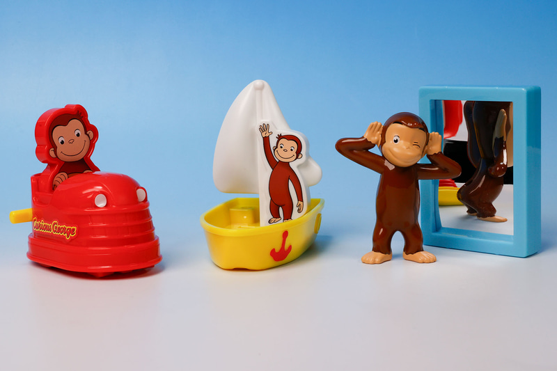 こちらが第1弾（1月12日～1月18日）のハッピーセット「おさるのジョージ」に登場するおもちゃ。写真左から「ジョージのドキドキドライブ」、「ジョージのグラスボートたんけん」、「ジョージのおもしろミラー」