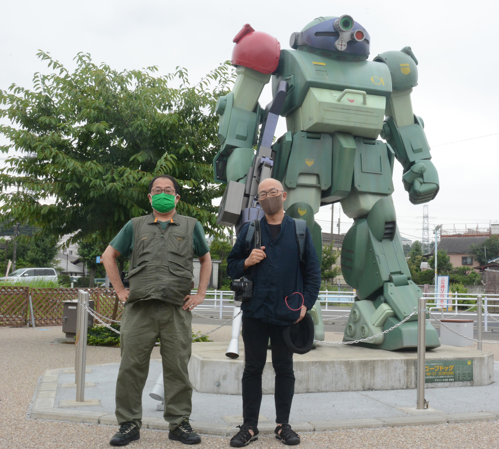 東京都稲城市の稲城長沼駅前にある「実物大スコープドッグ立像」。写真に写っている人物は記事制作に協力してもらったライターの池紀之氏と、杉山淳一氏