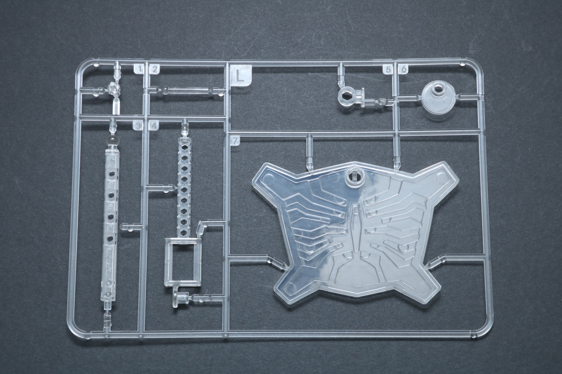 Lパーツ。クリアの成型色で台座パーツが封入。土台部分は「ジアース」のフェイス部分を模したデザインとなっている。