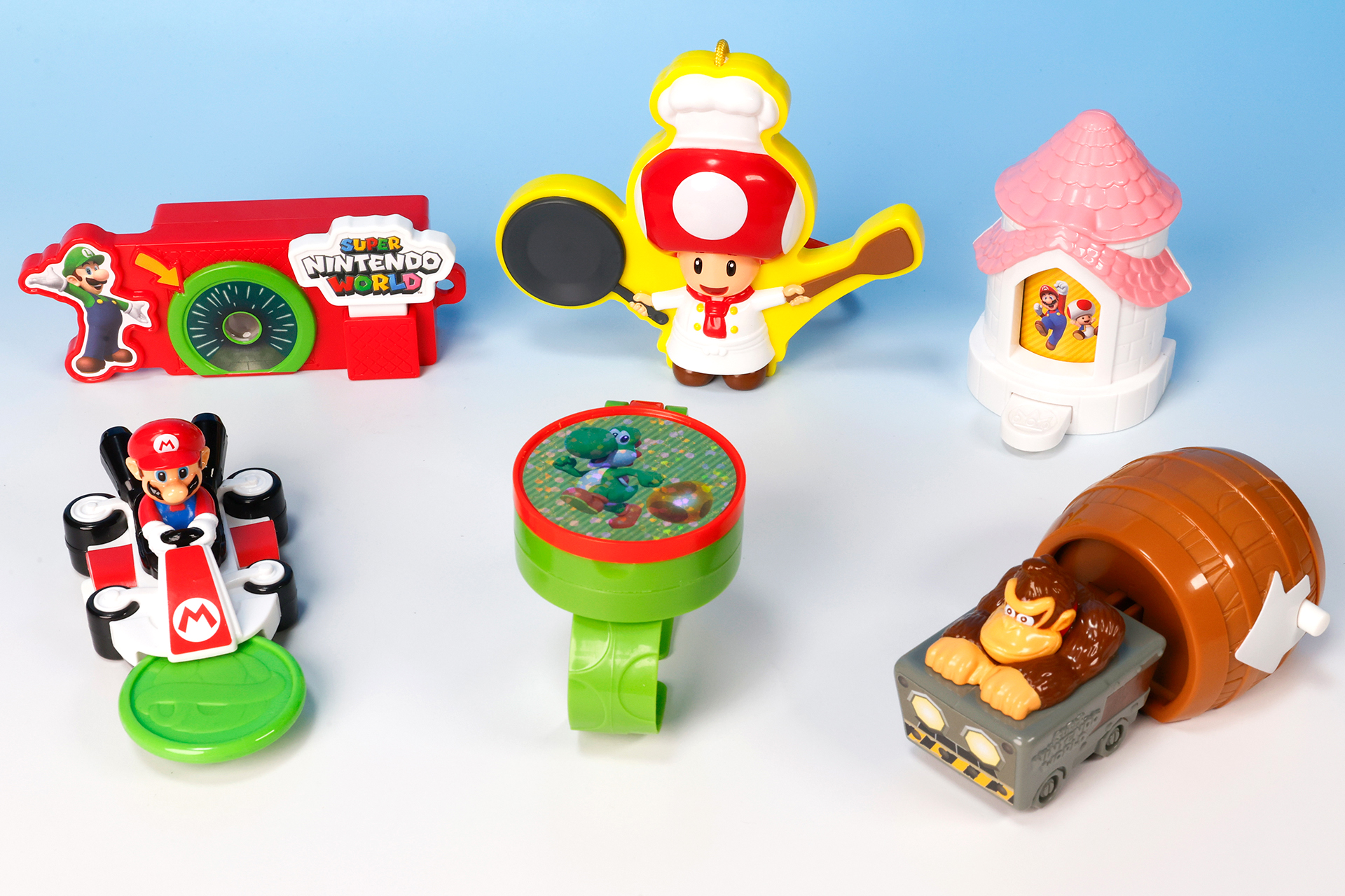 こちらが第1弾（7月12日～7月18日）のハッピーセット「ユニバーサル・スタジオ・ジャパン オールスターズ」に登場するおもちゃ。写真左上から「土管をのぞいてぼうけん！スーパー・ニンテンドー・ワールド」、「陽気におりょうり！シェフキノピオのわなげけん玉」、「だれに会えるかな？ピーチ城のルーレット」。写真左下から、「こうらをとばそう！マリオカート」、「タマゴをあつめよう！ヨッシーのブレスレット」、「ジャングルへ飛び出そう！ドンキーコングのトロッコ」