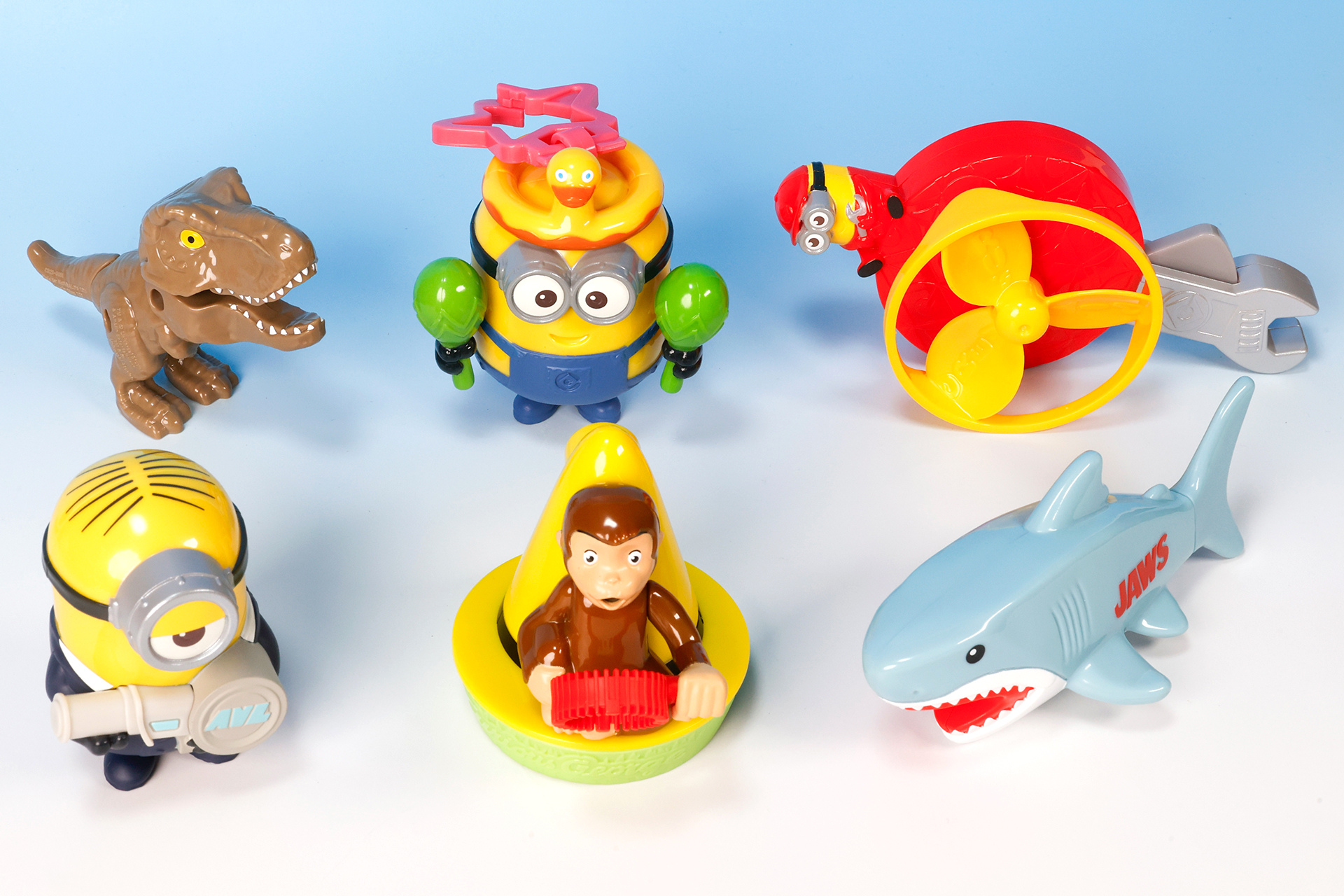 こちらが第2弾（7月19日～7月25日）のハッピーセット「ユニバーサル・スタジオ・ジャパン オールスターズ」に登場するおもちゃ。写真左上から「ガブっとキャッチ！ジュラシック・パーク T-レックス」、「シェイク！パーティミニオン」、「かぜをおこそう！ピットクルーミニオン」。写真左下から、「エージェントミニオンの水でっぽう」、「おさるのジョージのシャボン玉」、「ジョーズの水でっぽう」