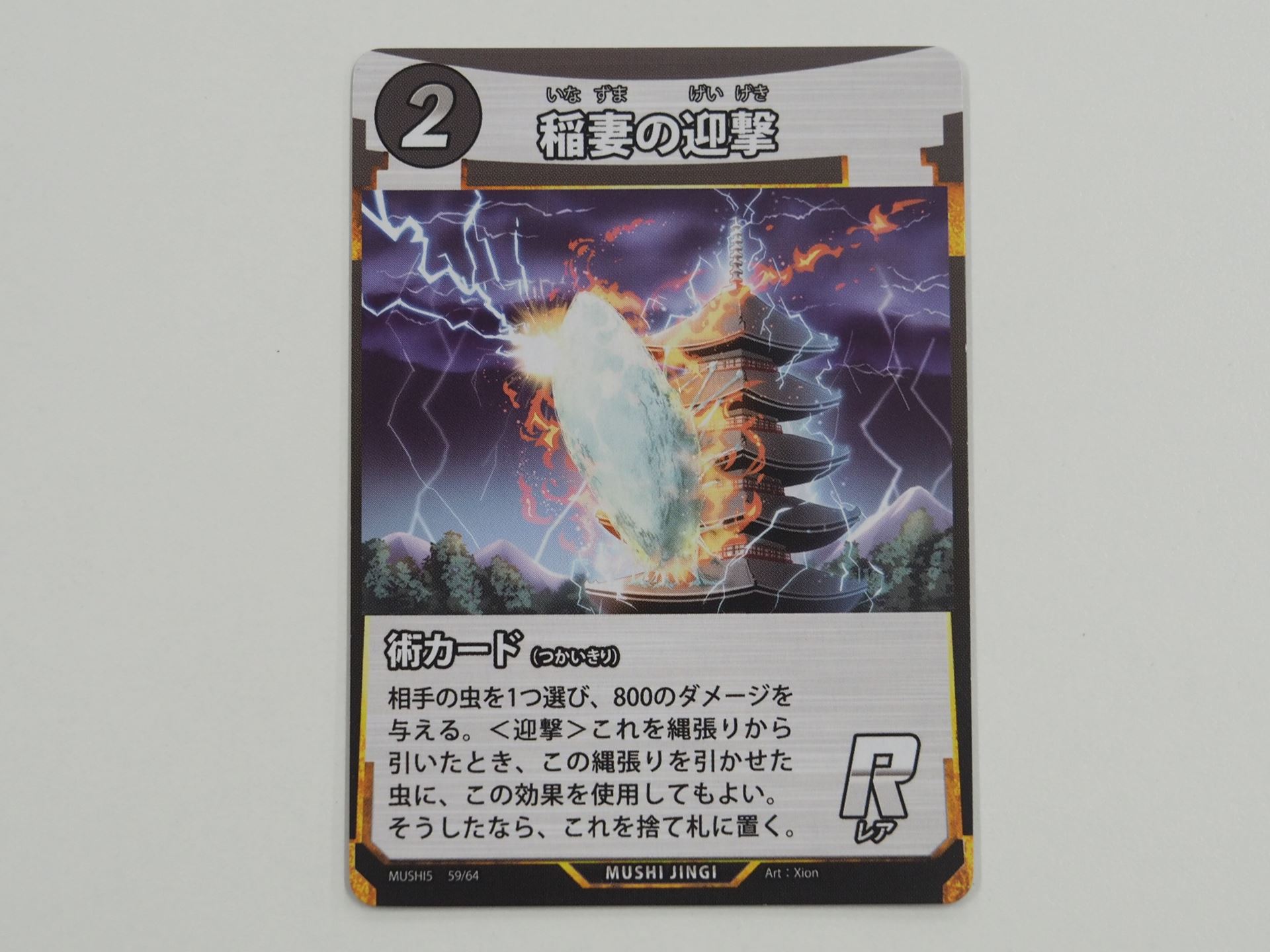 2コストのR術カード「稲妻の迎撃」。先行体験会で初出のカード。相手の虫に800ダメージを与える。また、縄張りから引いたときにその虫に効果を適用できる＜迎撃＞を持つ