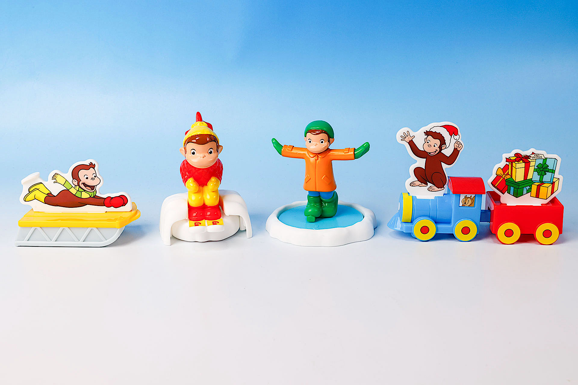 こちらが第1弾（12月13日〜12月26日）のハッピーセット「おさるのジョージ」に登場するおもちゃ。写真左から「ジョージのそりあそび」、「とびだせ！ジョージのスキー」、「くるくる！ジョージのスケートあそび」、「ジョージのクリスマスれっしゃ」