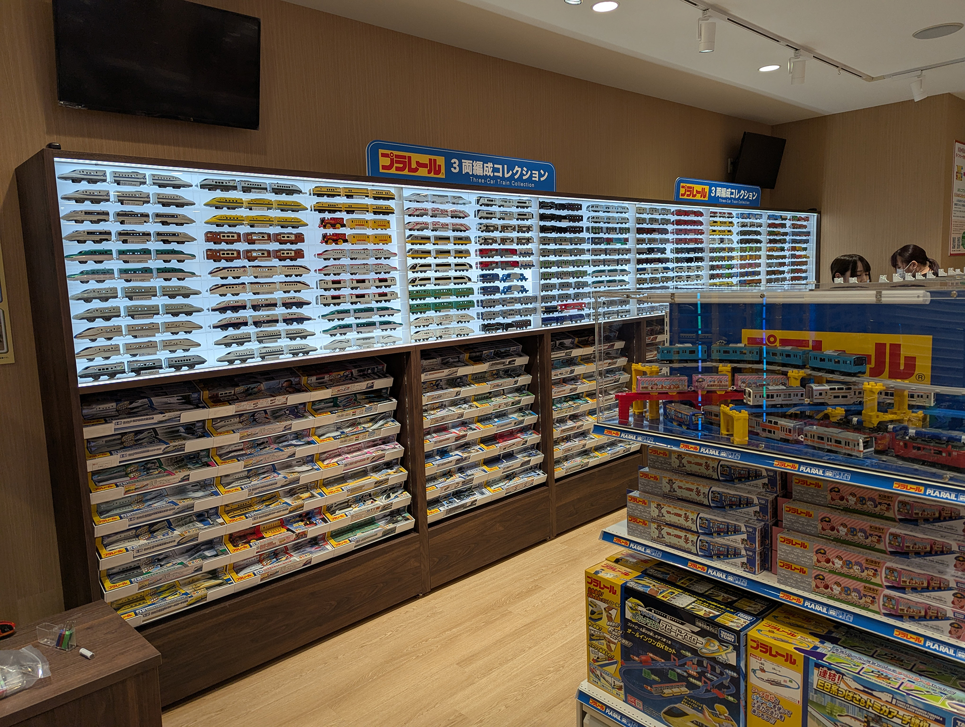 壁面には3両編成コレクションとして多くのプラレールの車両が3両編成で並べて展示されている。これらは現行製品なので、下部の棚から製品が購入可能だ