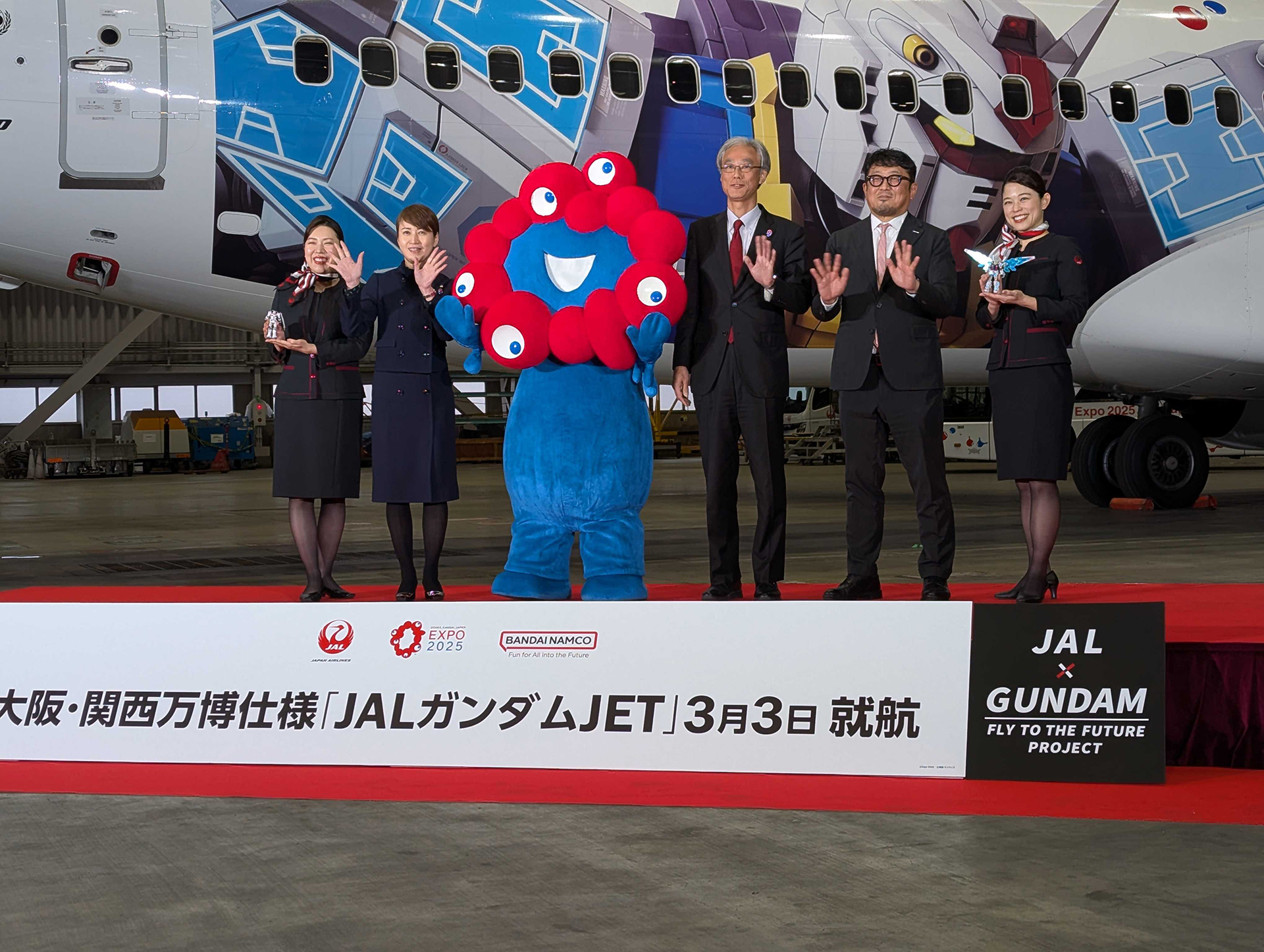 オープニングセレモニー。ミャクミャクの左となりが日本航空 常務執行役員 西日本支店長 宮坂 久美子氏。右となりが2025年日本国際博覧会協会 副事務総長 高科 淳氏と、バンダイナムコホールディングス 取締役 桃井 信彦