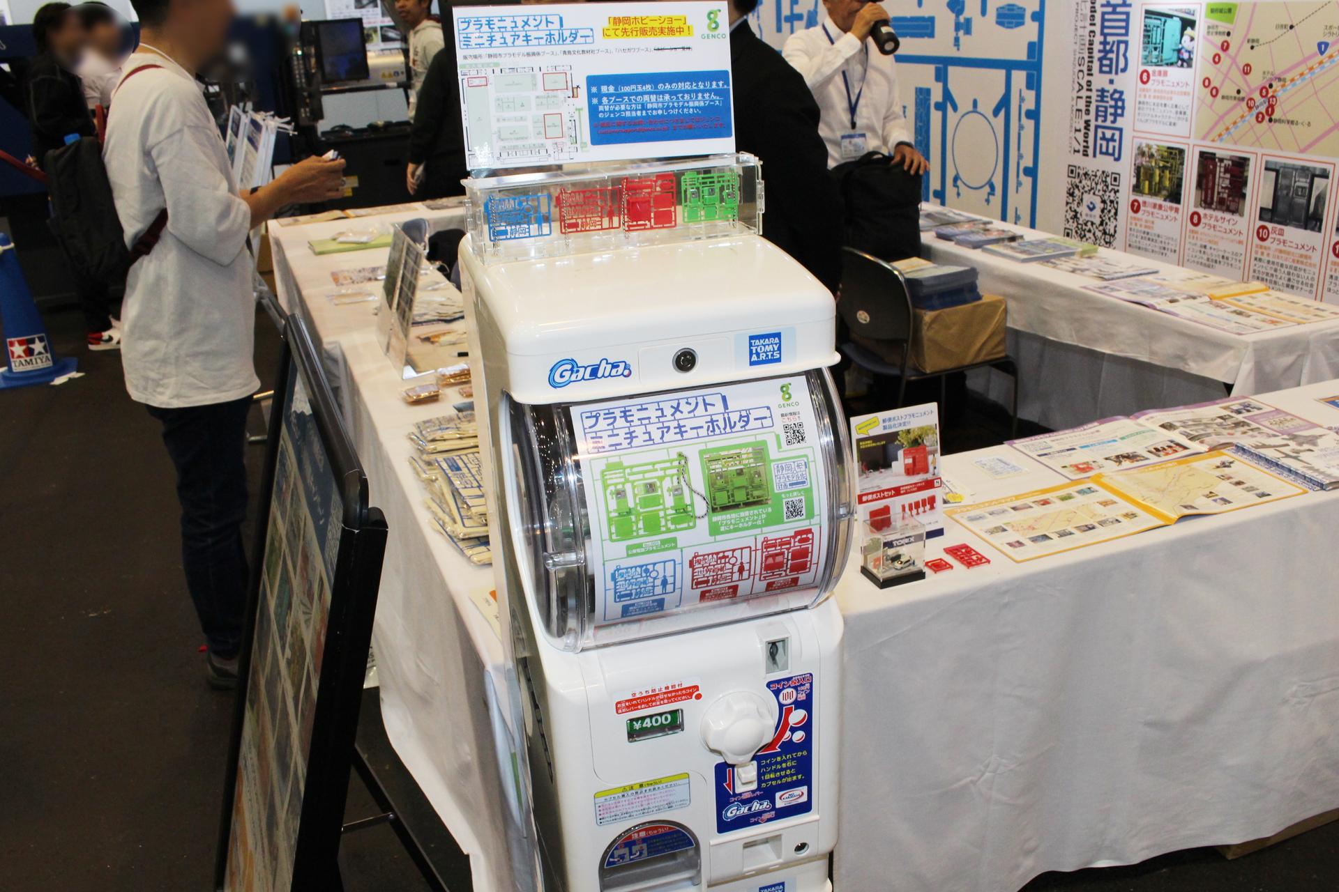 ホビーショーのハセガワ、アオシマ、静岡市プラモデル復興係、主催本部の各ブースに自販機を設置。一般公開日にももちろん販売される。両替は写真の静岡市プラモデル復興係のブースでお願いしよう