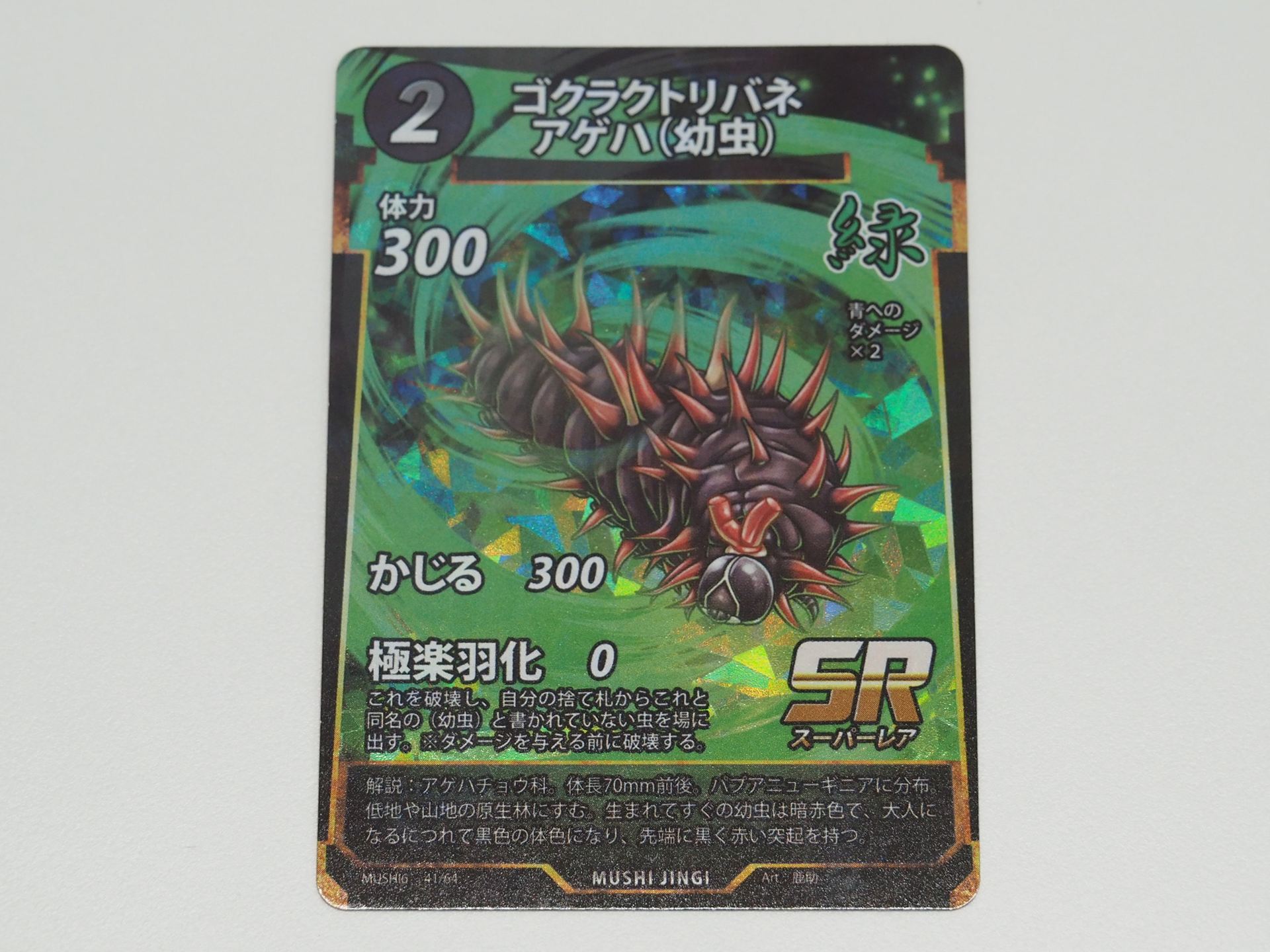 緑2コストのSRカード「ゴクラクトリバネアゲハ（幼虫）」。先行体験会で初出のカード。破壊すると、捨て札から「ゴクラクトリバネアゲハ」を場に出せる技「極楽羽化」を持つ