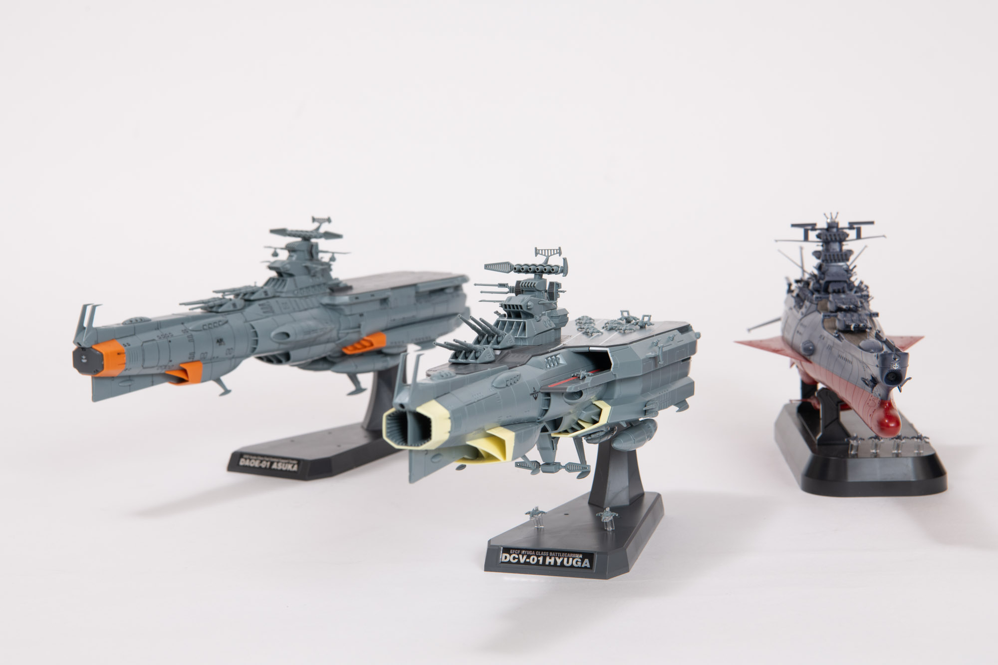 『ヤマトよ永遠に REBEL3199』1/1000スケール最新キットとなる「1/1000 地球防衛軍 ヒュウガ級 戦闘航宙母艦 DCV-01ヒュウガ」（写真中央）。同スケールで発売中の「1/1000 宇宙戦艦ヤマト3199(第3次改装型：参戦章叙勲式典記念塗装）」（写真右）、「1/1000 地球防衛軍アスカ級補給母艦/強襲揚陸艦 DX」（写真左）と並べて楽しめる。
