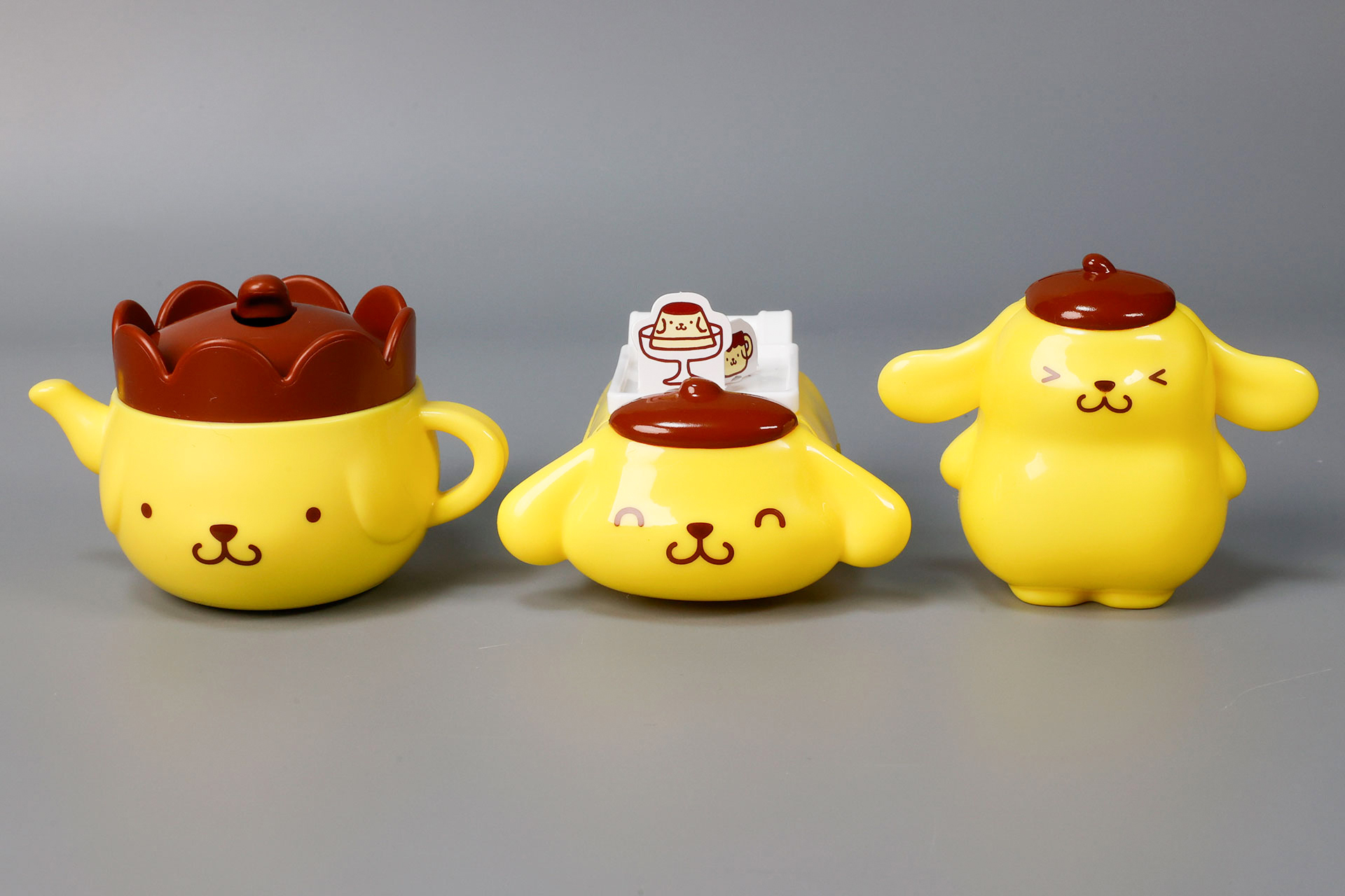 こちらが第1弾（1月16日〜1月22日）のハッピーセット「ポムポムプリン」に登場するおもちゃ。写真左から「ポムポムプリン ティーポット型 こものいれ」、「ポムポムプリン ころころカート」、「ポムポムプリン 耳がパタパタ えんぴつキャップ」