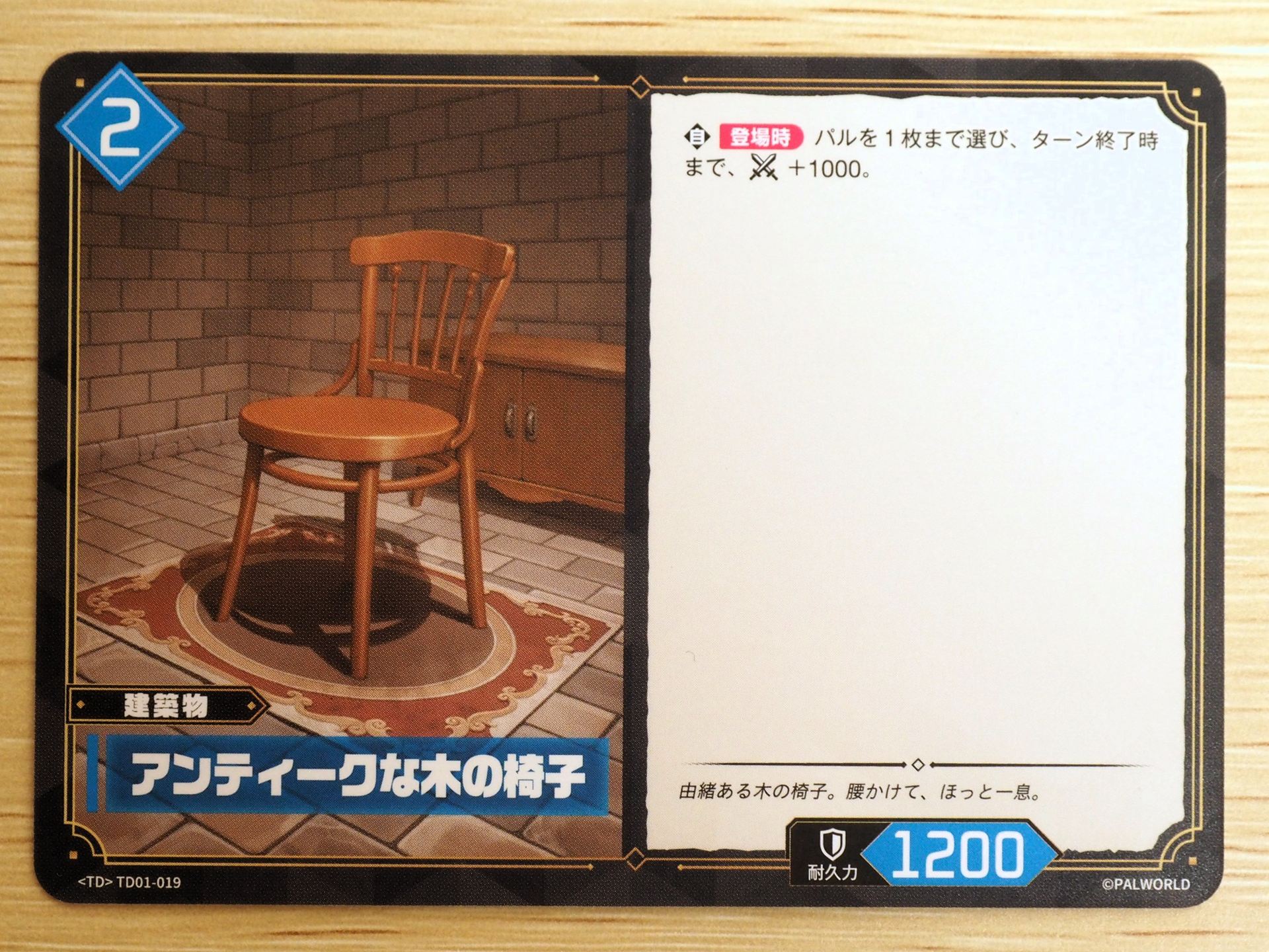 青2コストの「建築物カード: アンティークな木の椅子」。登場時に、パルを1枚まで選び、ターン終了時まで戦闘力を＋1000できる