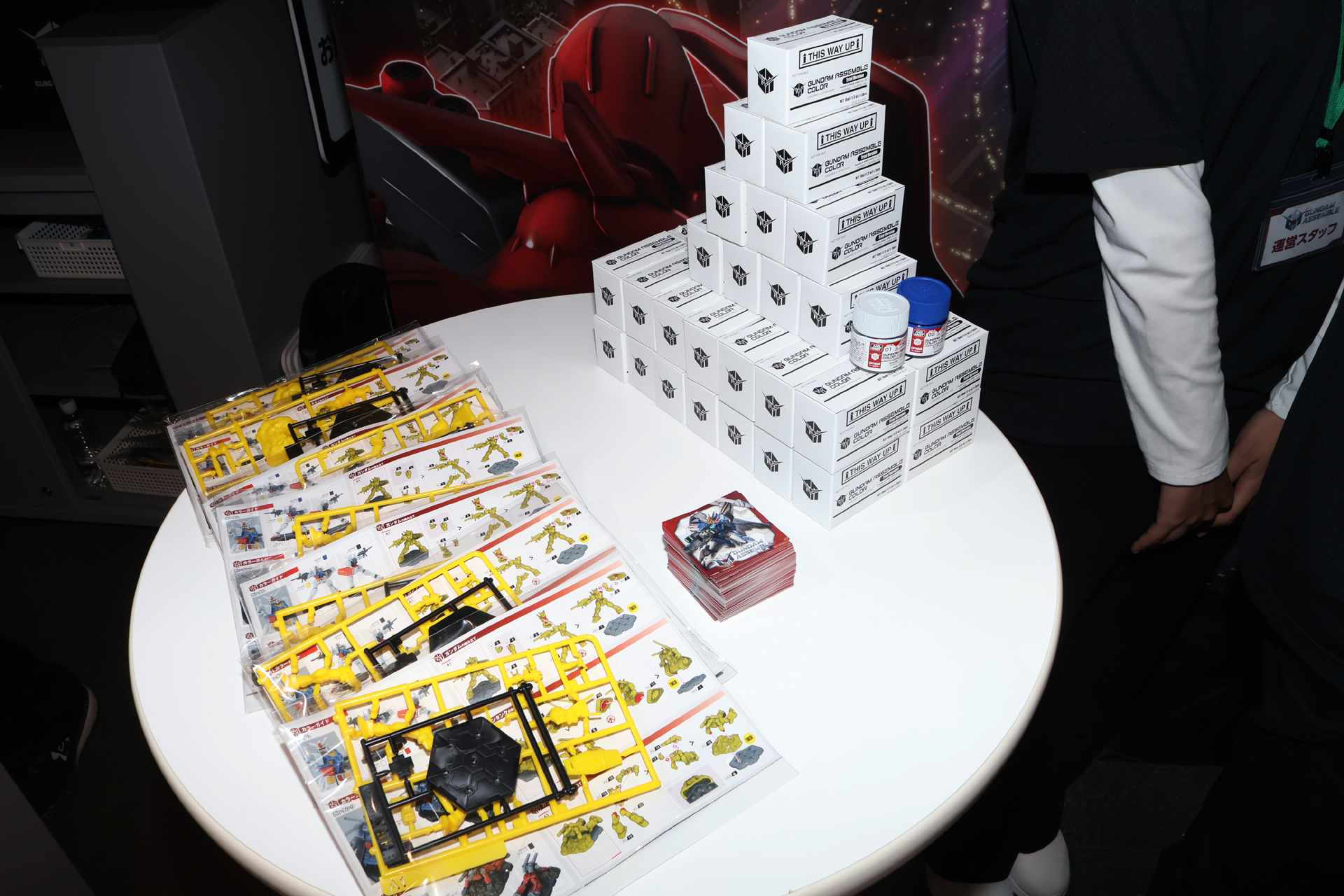 SNSフォローで限定カラーのミニチュア（左下）が、公式プラットフォーム「BANDAI TABLETOP GAMES」の登録で「GUNDAM ASSEMBLE COLOR」2色のサンプル（右上）が、そしてSNSへの投稿で特製ステッカー（中央）がそれぞれプレゼントされる